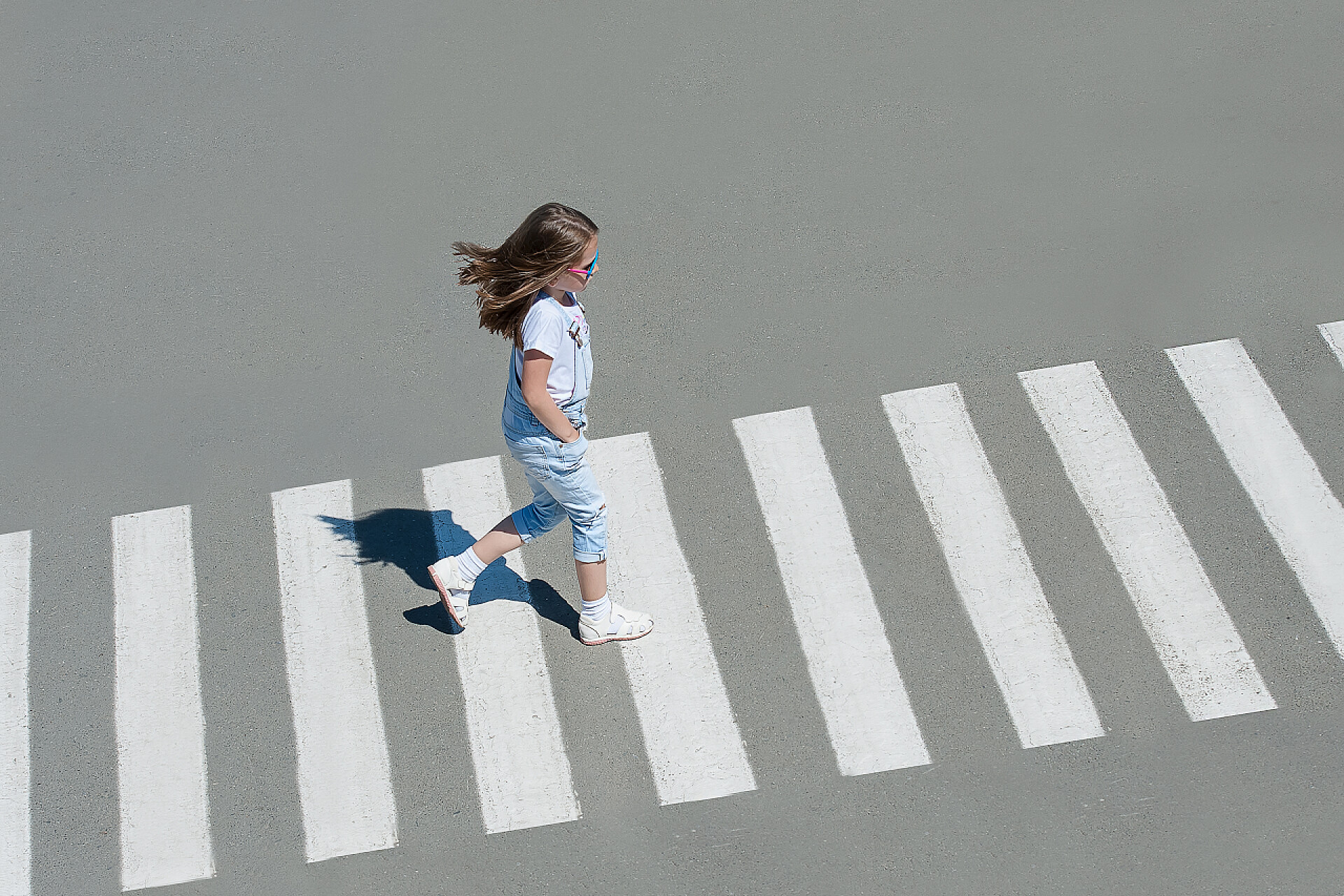过马路的小女孩夏天在街上过马路的穿时尚服装的小女孩过马路。从顶部视图。斑马线的阴影