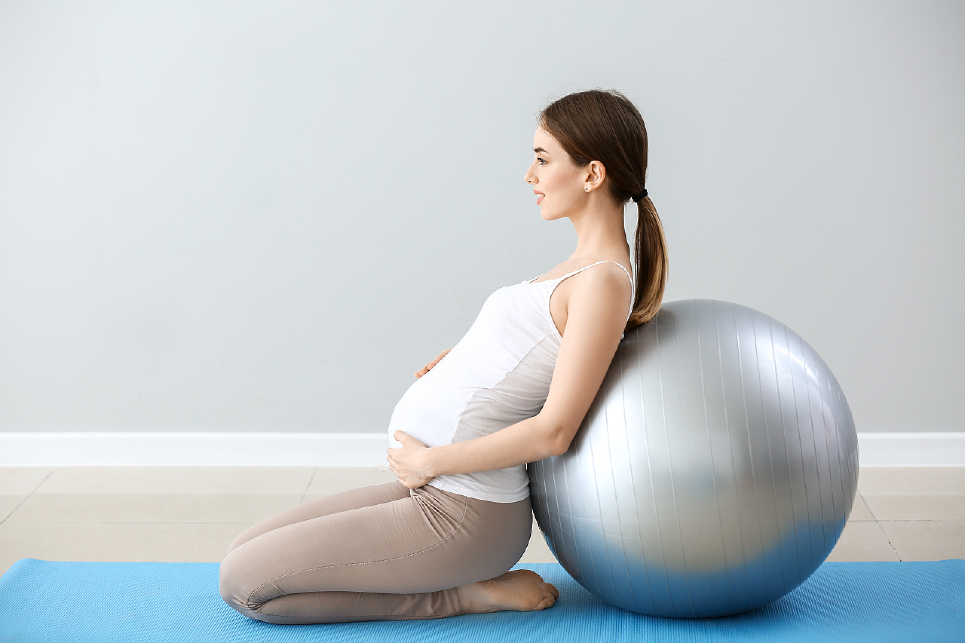 美丽的孕妇与健身球训练附近的灰色墙壁美丽的孕妇与健身球训练附近的灰色墙壁