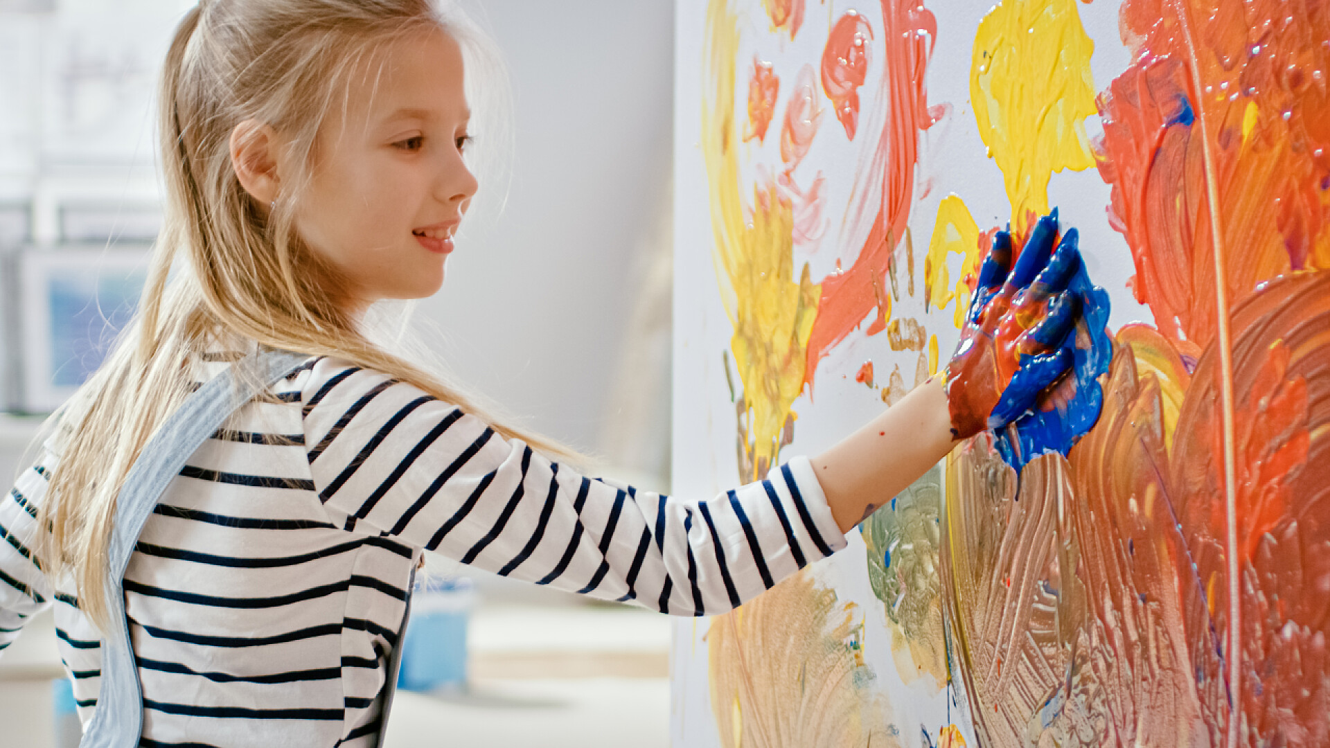 小女孩双手浸在生动的油漆画里快乐的小女孩,双手浸在生动的油漆画在墙上五颜六色的抽象。她有乐趣和笑。家正在装修.