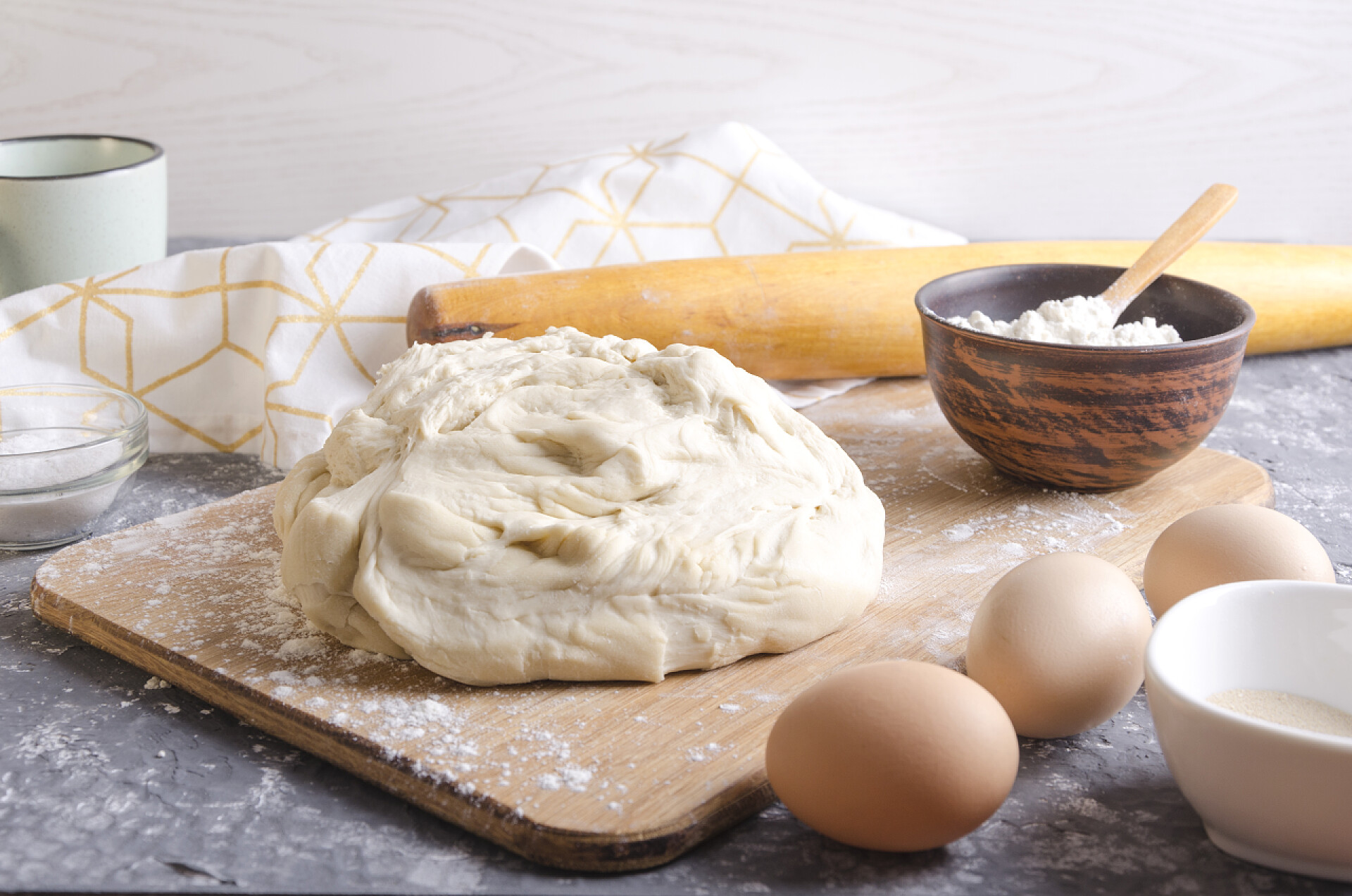 木板上的面团准备在木板上的披萨面团。用于大自制面团的配料。灰色厨房桌上的牛奶、鸡蛋、面粉、滚针