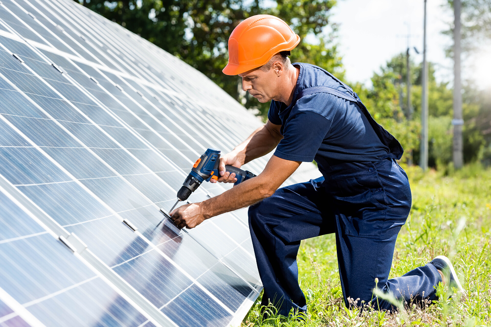 英俊的工程师在使用钻头英俊的工程师在T恤和橙色安全帽使用钻头 