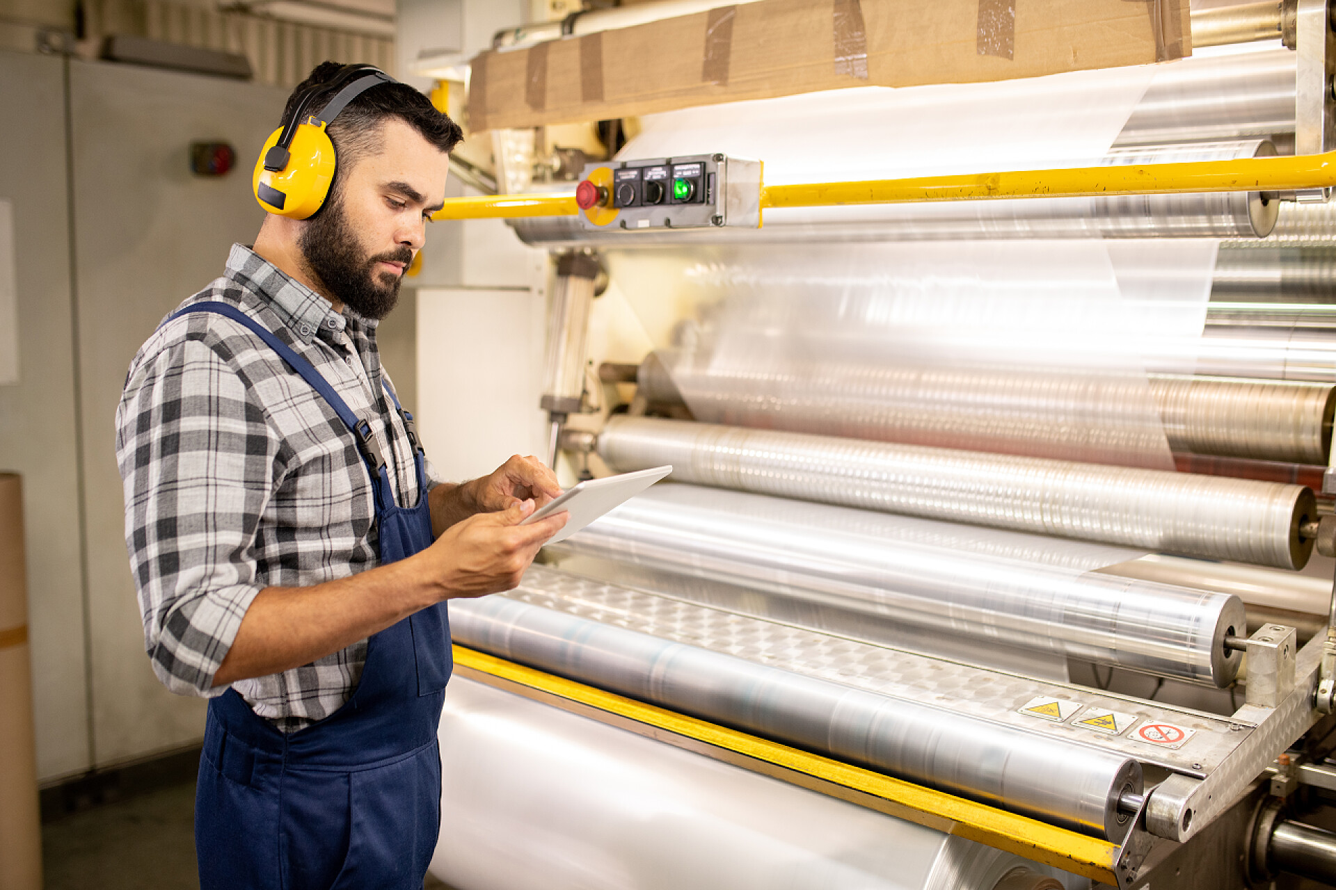 建筑工程师正在观察施工材料年轻的认真的质量控制工程师使用平板电脑检查加工材料的参数，同时站在生产机器