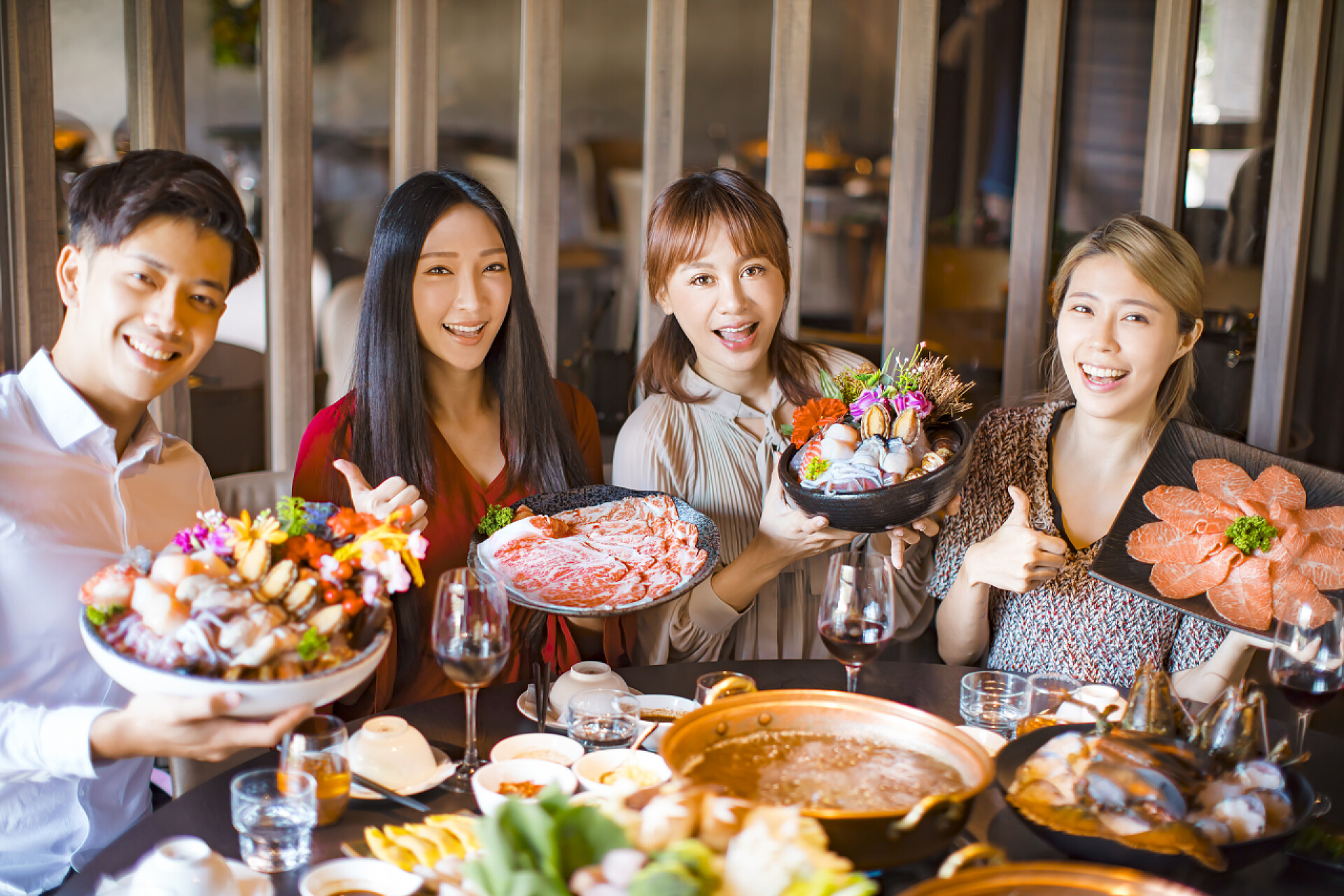 朋友在火锅餐厅吃饭年轻的朋友在火锅里展示海鲜牛肉和猪肉片 