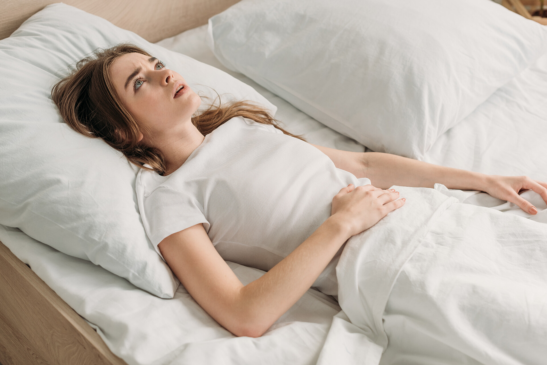 肚子疼的女孩躺在床上休息忧心忡忡的女孩躺在床上抬起头来，感到肚子痛