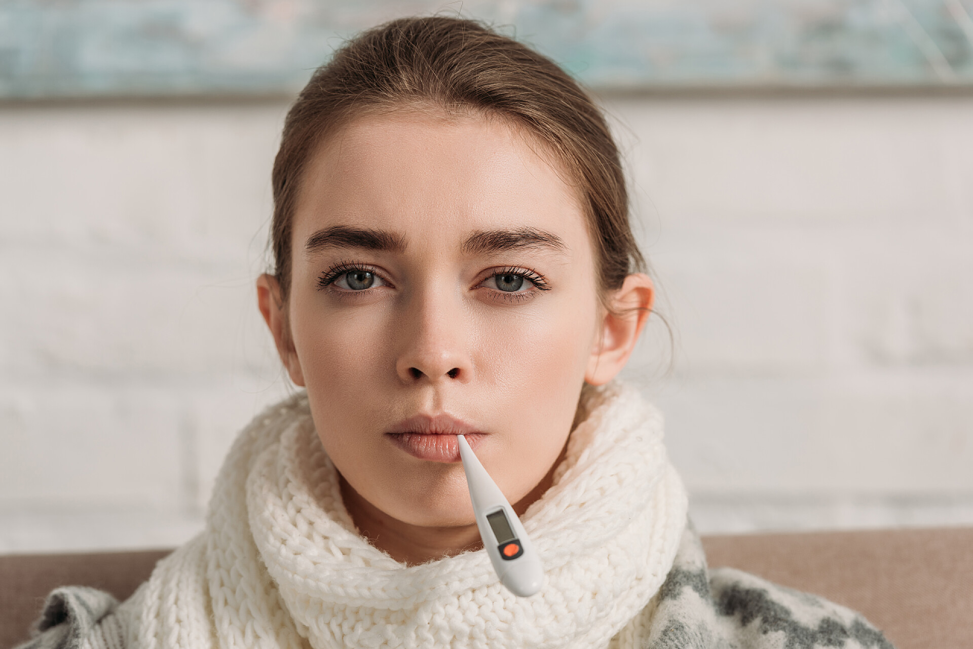 女孩测量体温生病的女孩脖子上缠着围巾，一边看着相机一边测量温度