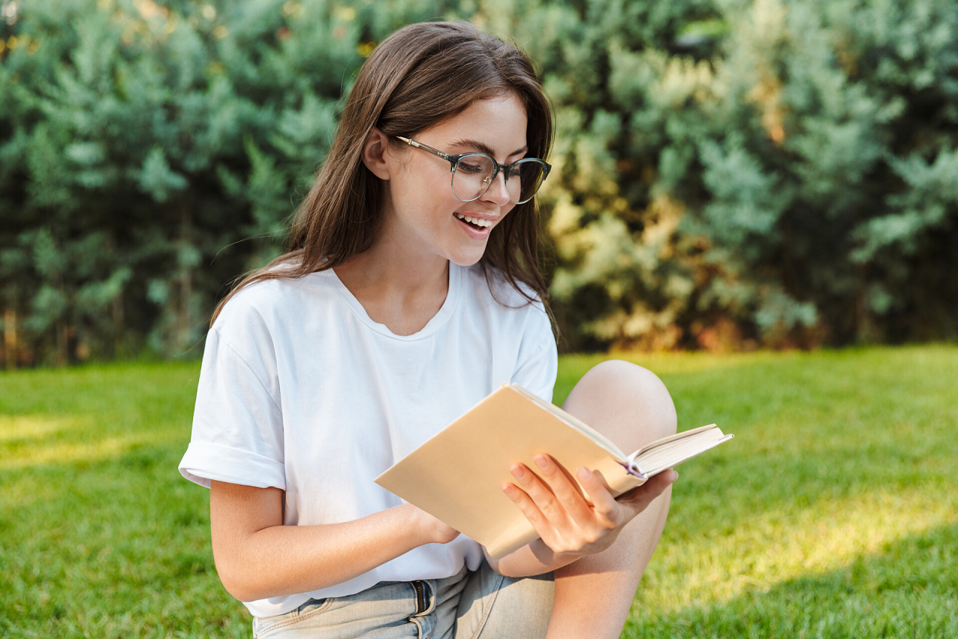 年轻女孩坐在公园看书微笑着年轻女孩读一本书