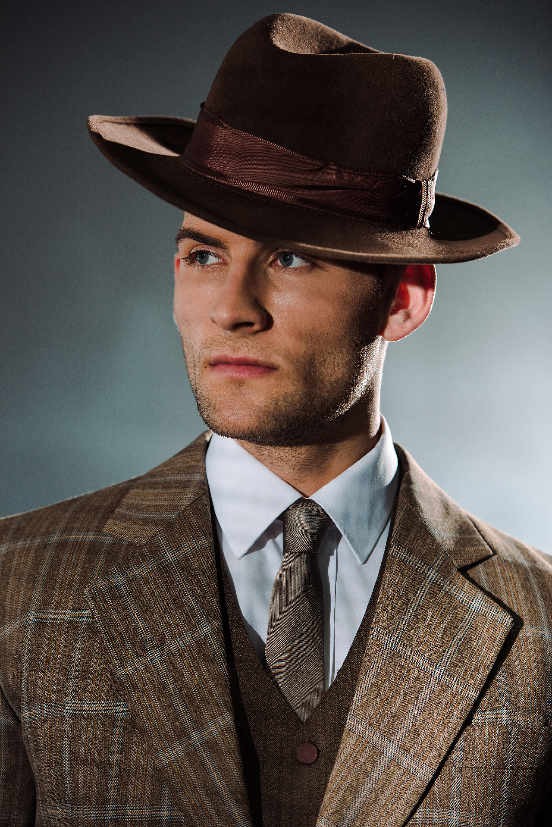 灰色背景上带牛仔帽的男人戴帽子、身穿黑色西服的英俊男子 