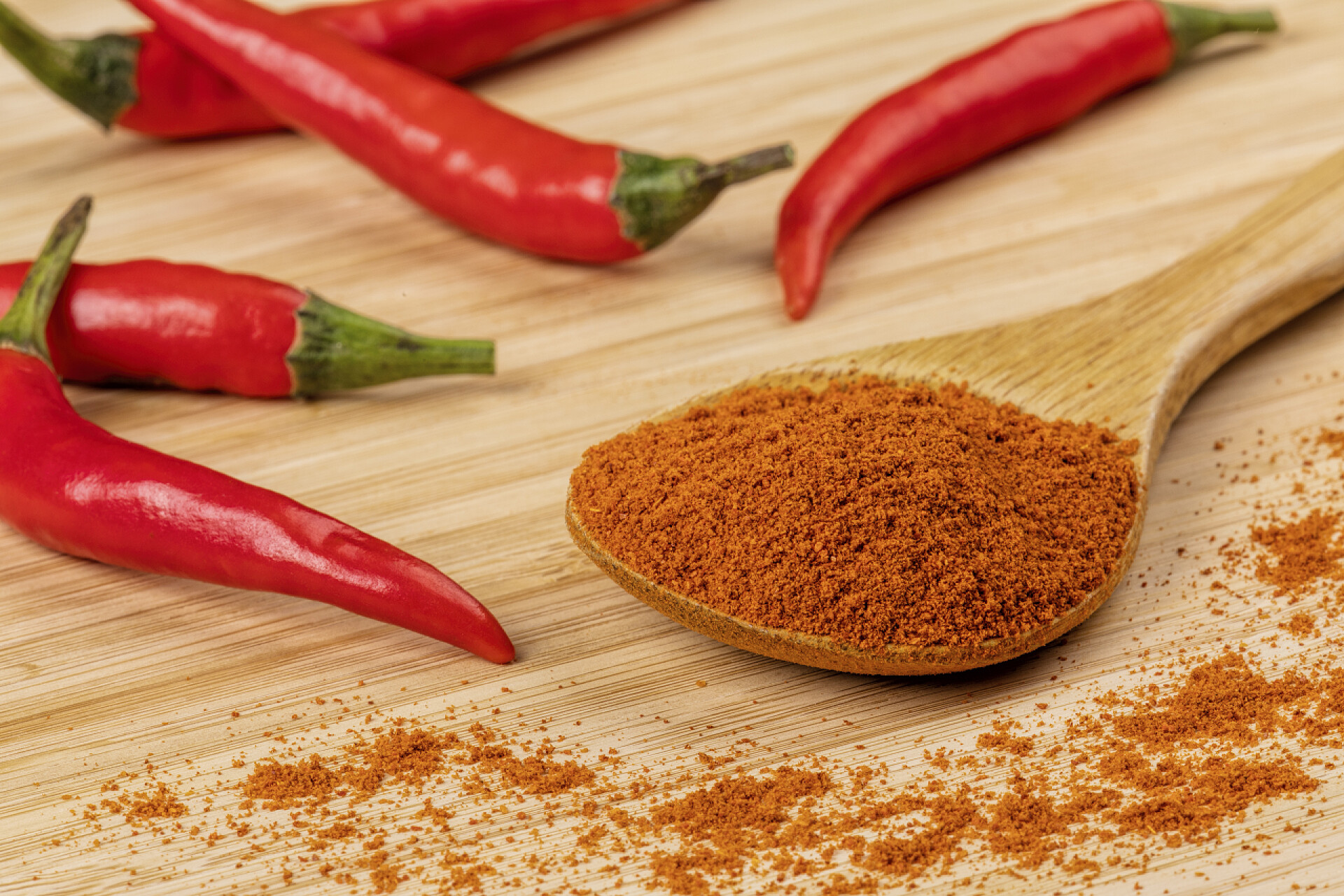 木桌上的新鲜辣椒和辣椒粉一汤匙奇利粉放在木制背景上