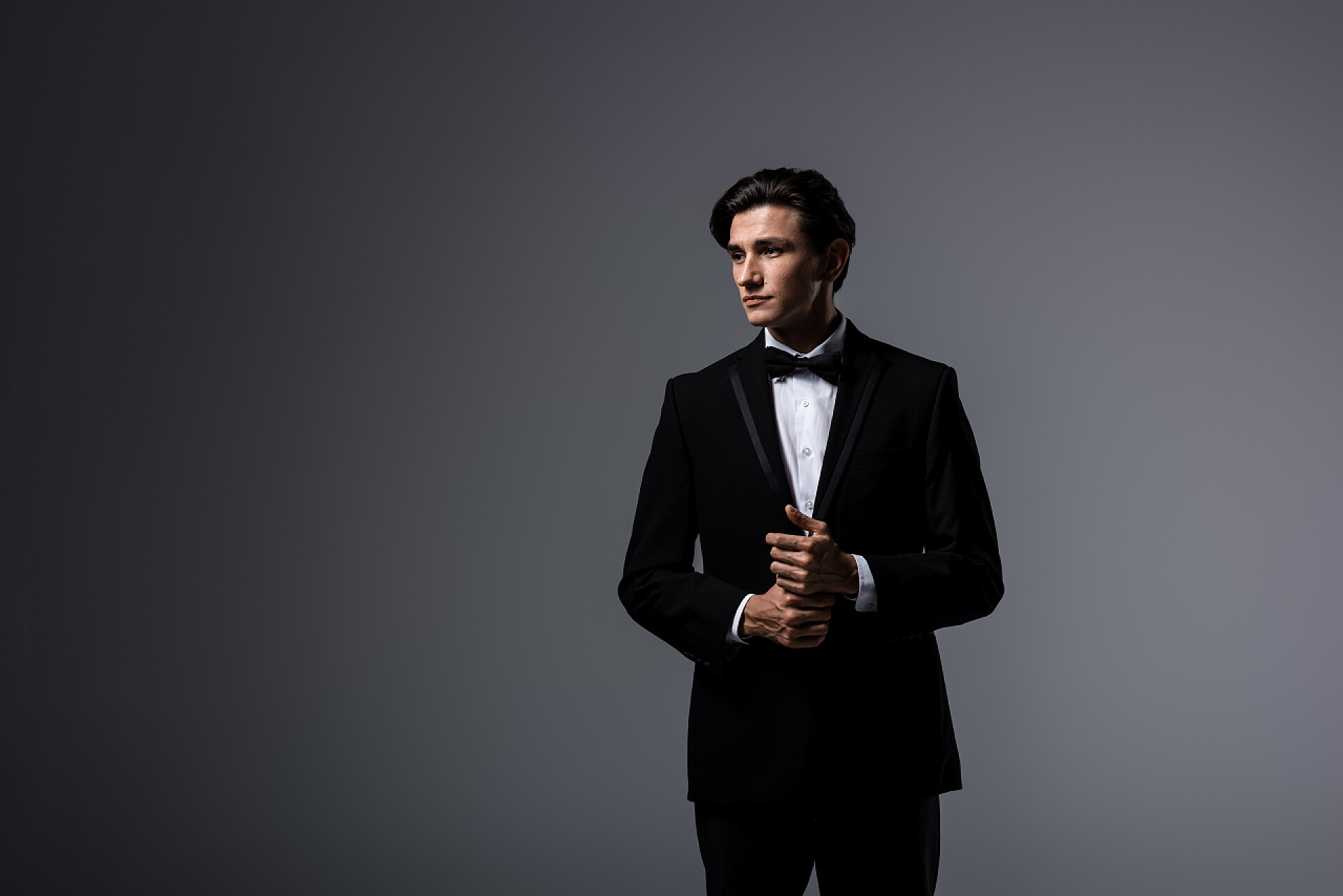 灰色背景上穿西服的男人穿着黑色西服打着蝴蝶结的英俊男人，与灰色隔离