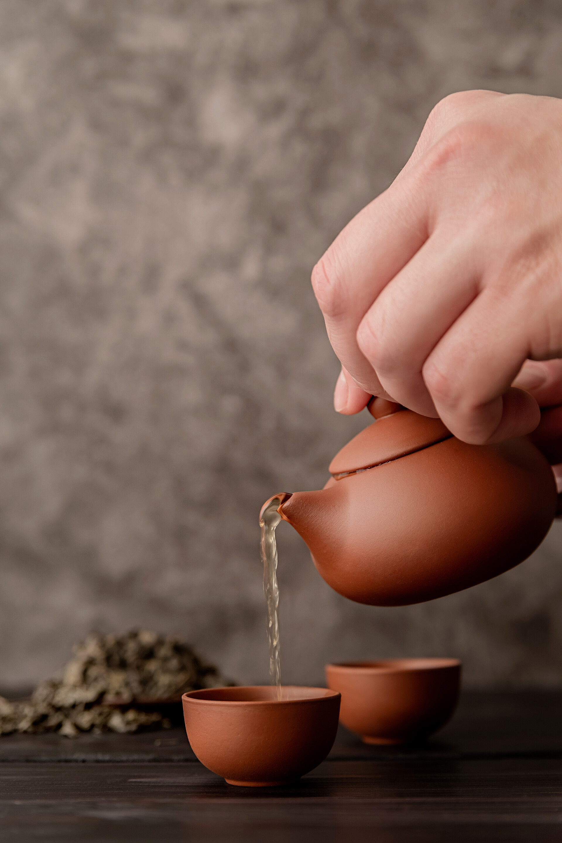 深色背景中一个男人正在倒茶男性手将茶倒入茶杯前视镜深色背景