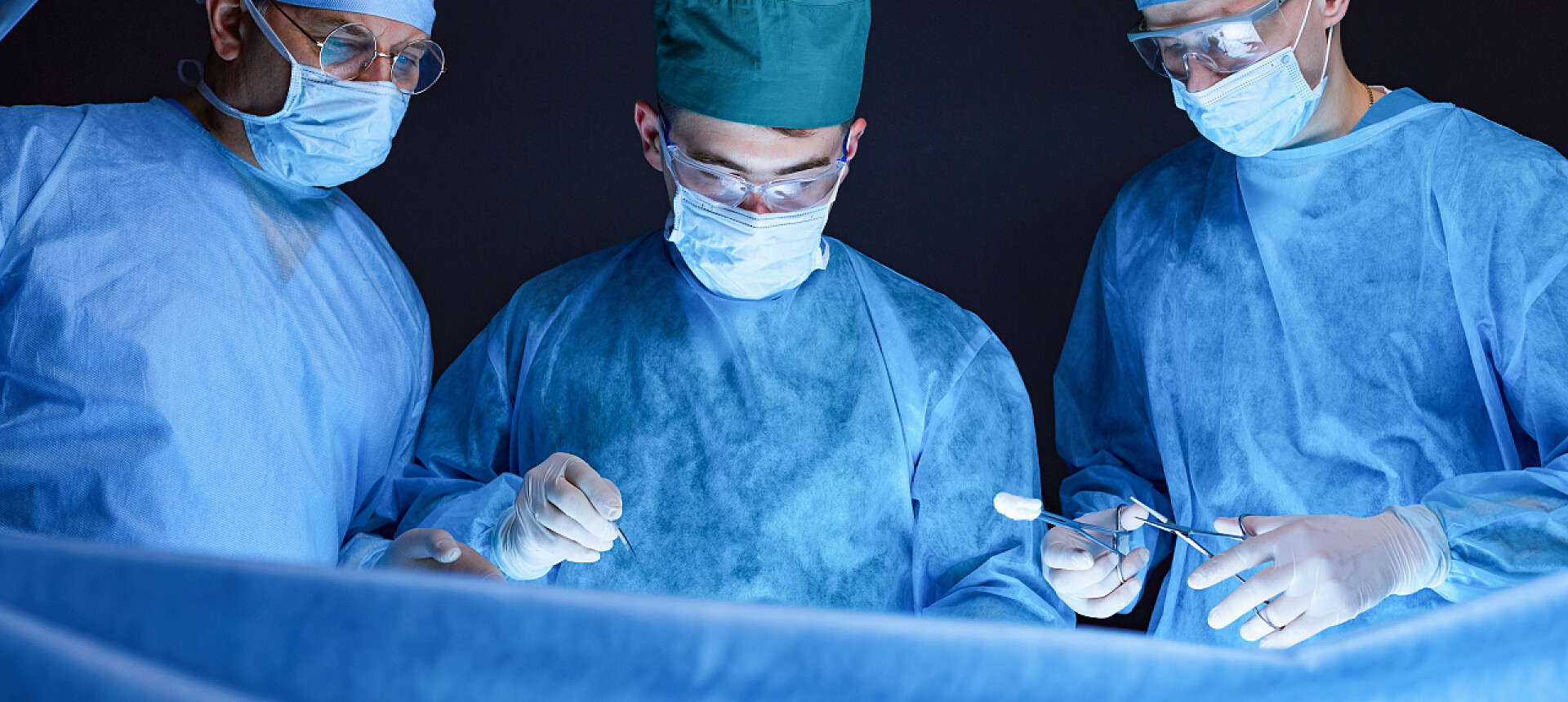 手术室中外科医生正在做手术在手术室工作的一组外科医生用蓝色调.执行业务的医疗小组