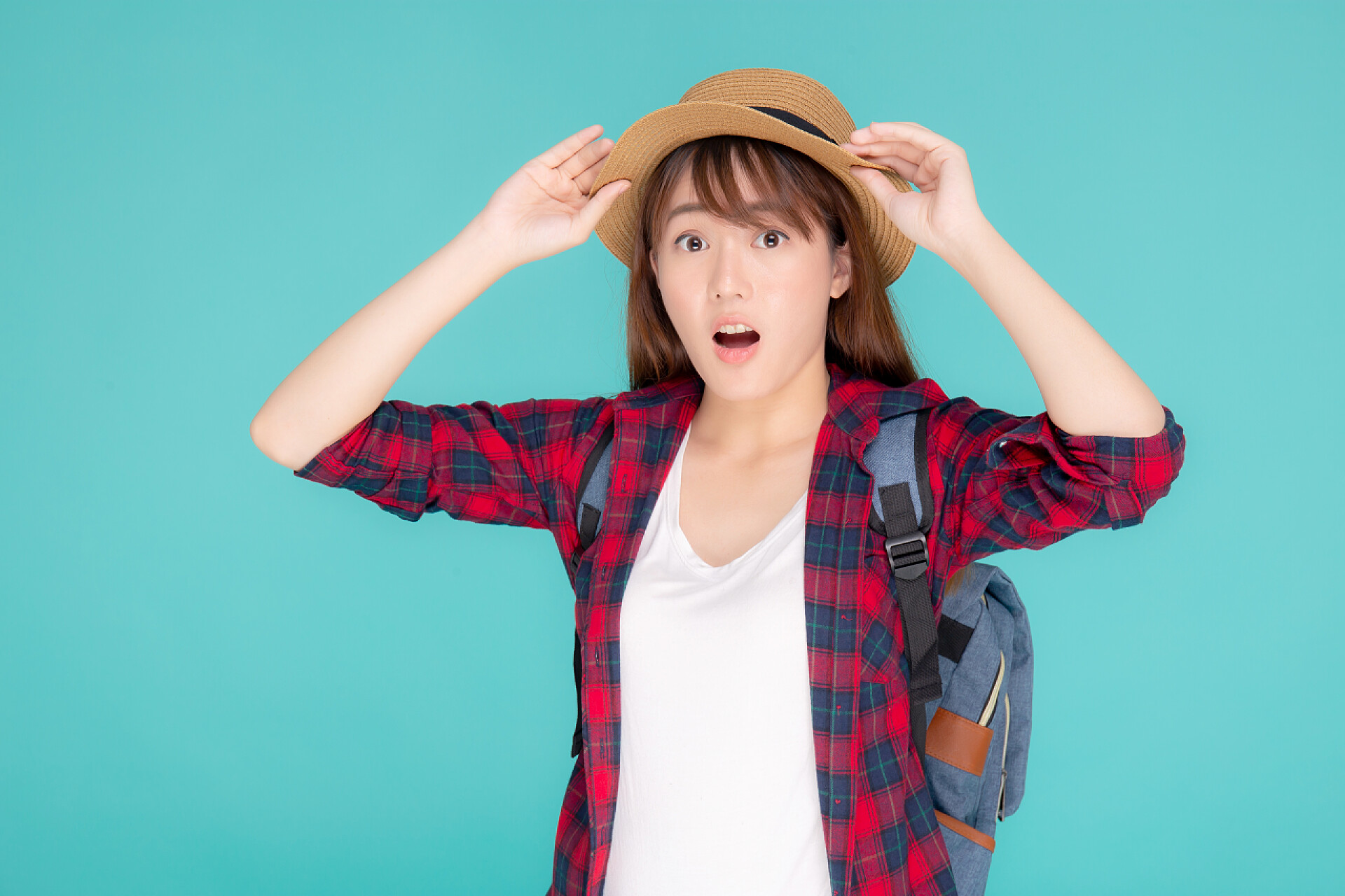 蓝色背景中一个女人背着包戴着帽子露出惊讶的表情美丽的肖像画年轻的亚洲女人笑着惊奇地穿上了衣服