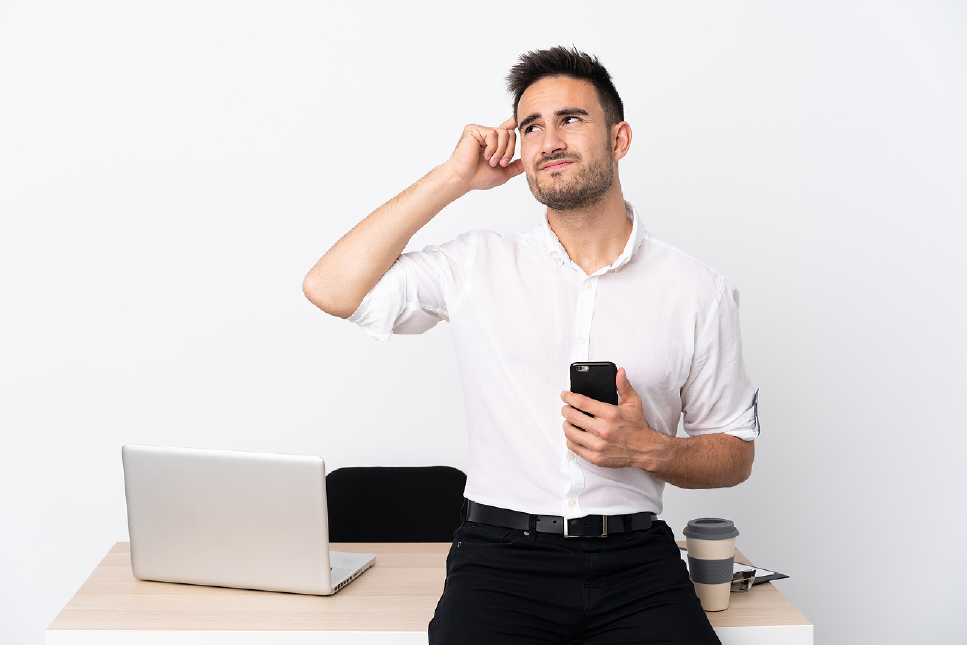 办公室里一个年轻的商人拿着手机满脸疑惑年轻的商人，在工作场所拿着手机，满脸疑惑，表情混乱