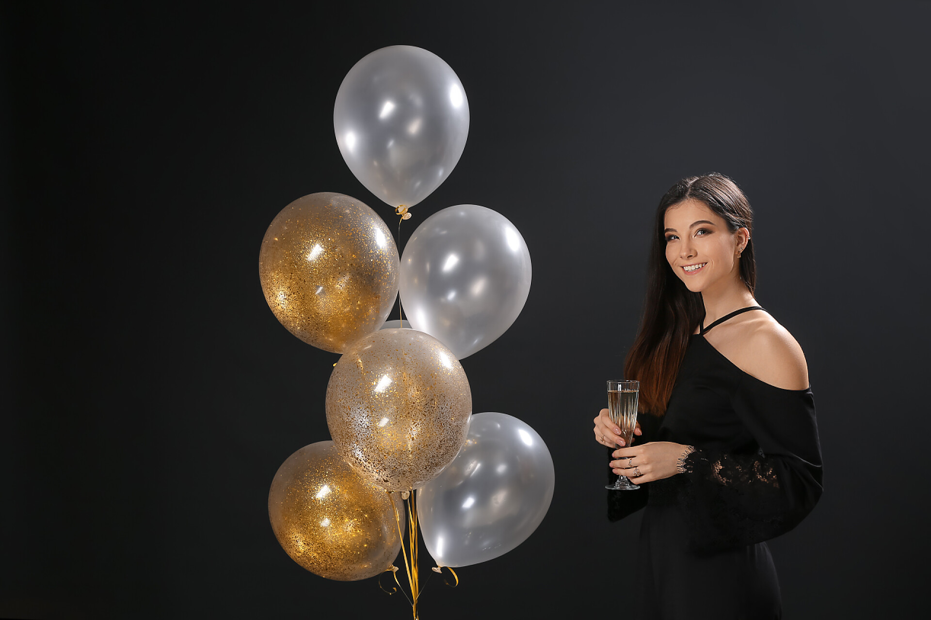 黑色背景上一个年轻貌美的女人和气球穿着深色背景的气球和香槟的年轻貌美女人