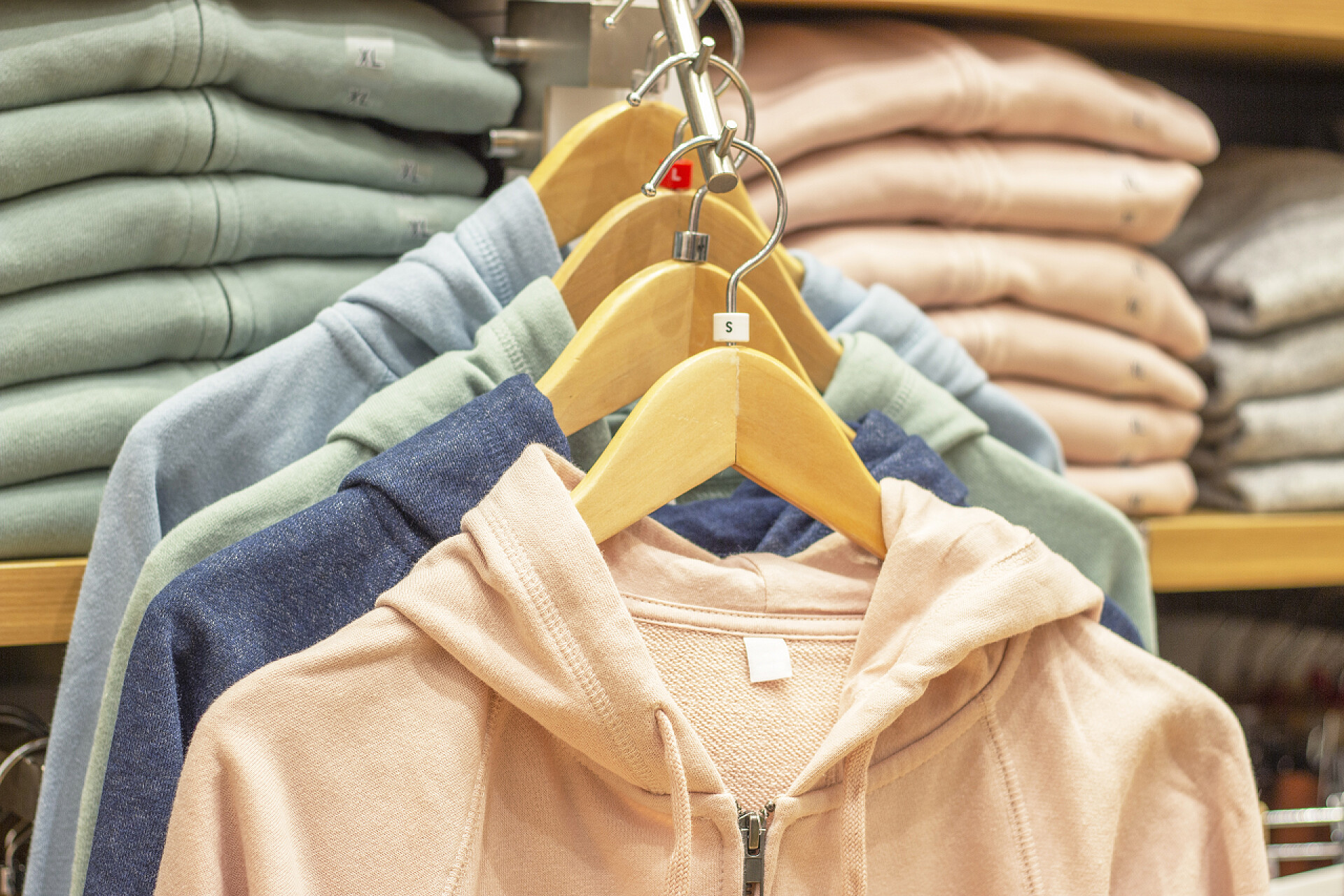 挂在衣架上的衣服Multicolored hoody hang on hangers opposite shelves with clothes in store.