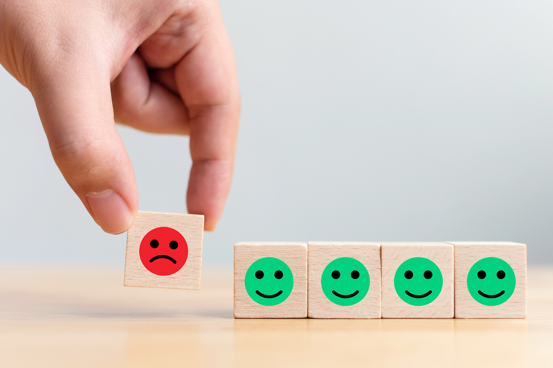 桌上画了绿色笑脸的木块和手拿画了悲伤的红色脸颊木块与图标面对情感的快乐与悲伤，别具一格，思维迥异，独树一帜，脱颖而出