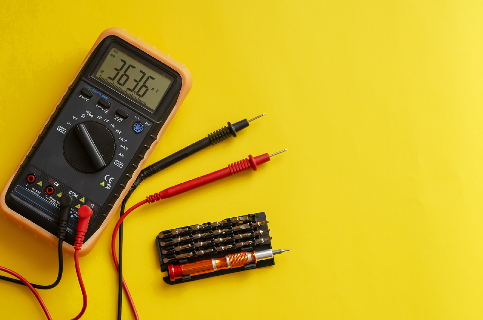 黄色背景上的电表检测仪用于螺丝刀的万用表和一组位元。典型的万用表可以测量电压、电流和电阻.工业背景。从上方的角度射击。软焦点.