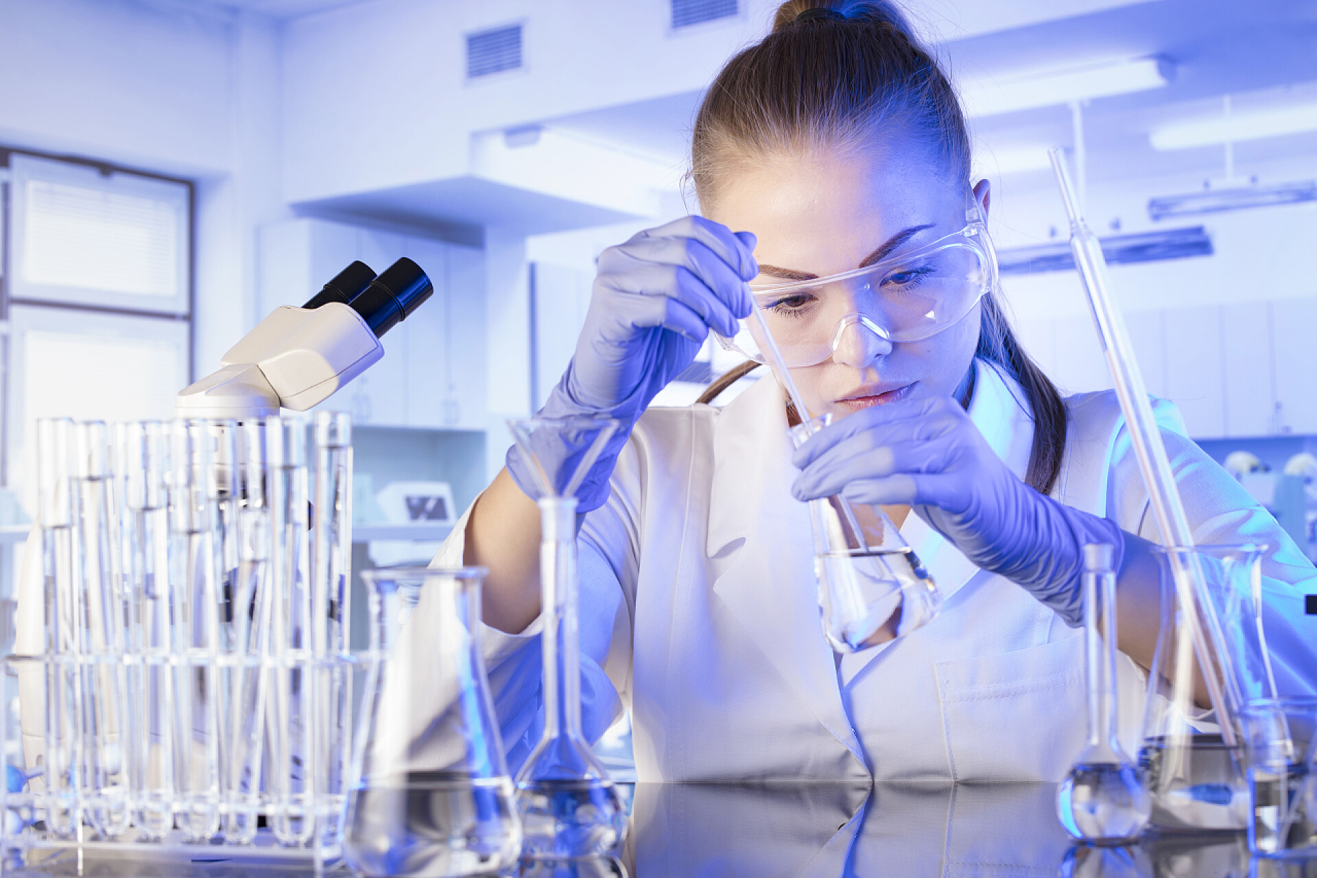 在实验室做实验的科学家实验室内部。科学研究概念。年轻科学家在现代实验室进行实验和使用显微镜.玻璃管和烧杯.