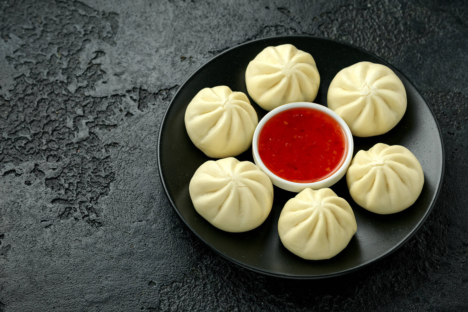黑盘上的蒸包和辣酱用鸭肉和辣椒酱包在黑盘上的蒸包