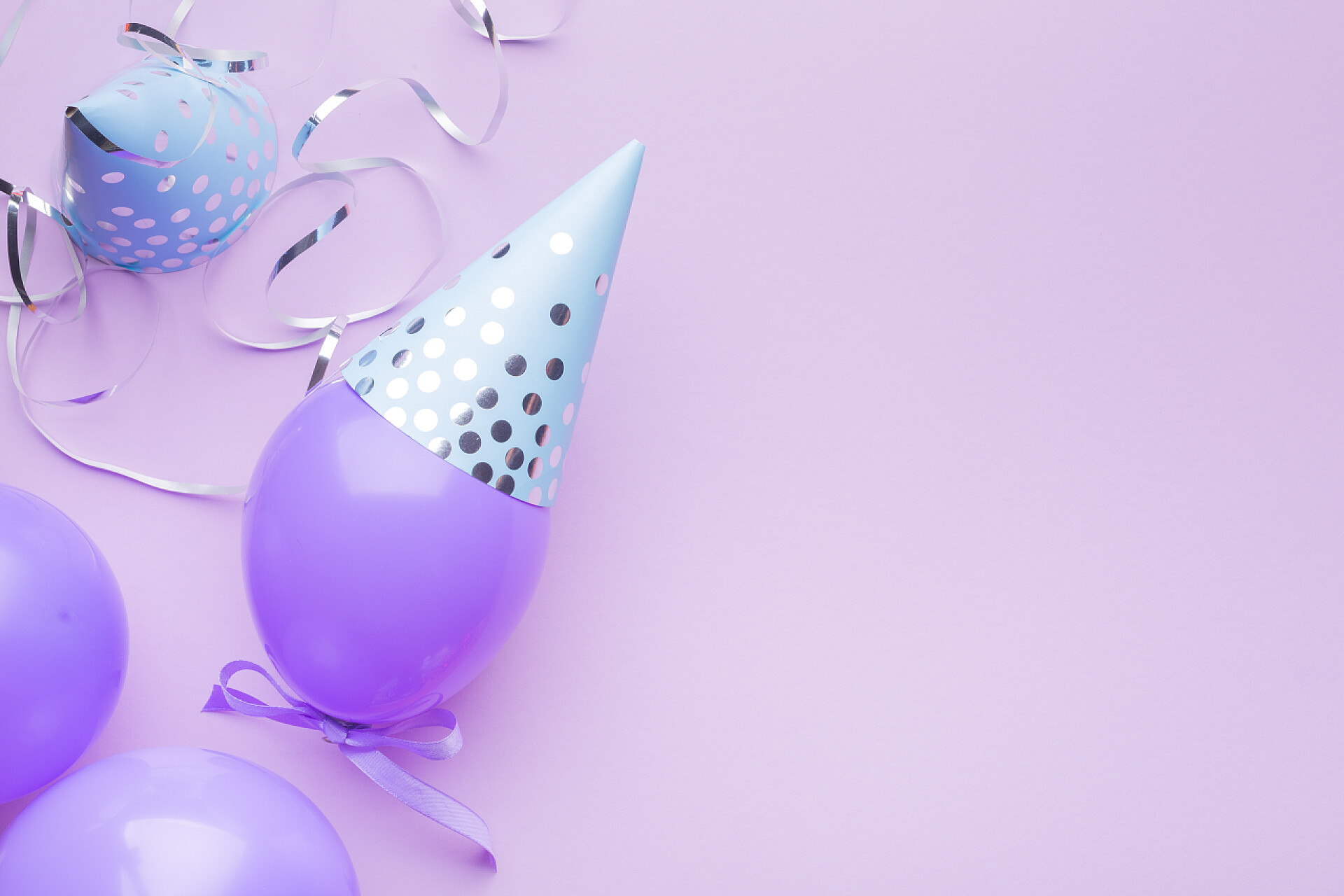 紫色背景上的紫色气球戴着蓝色的帽子蓝色的帽子，紫色的球和银色的蛇纹石在紫色的纸的背景。度假背景。复制空间，顶部视图.