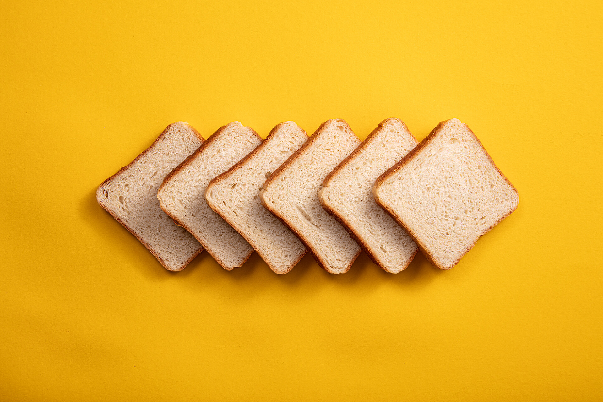 黄色背景上的正方形面包正方形面包顶视图.早餐面包切片后的明亮的黄桌背景
