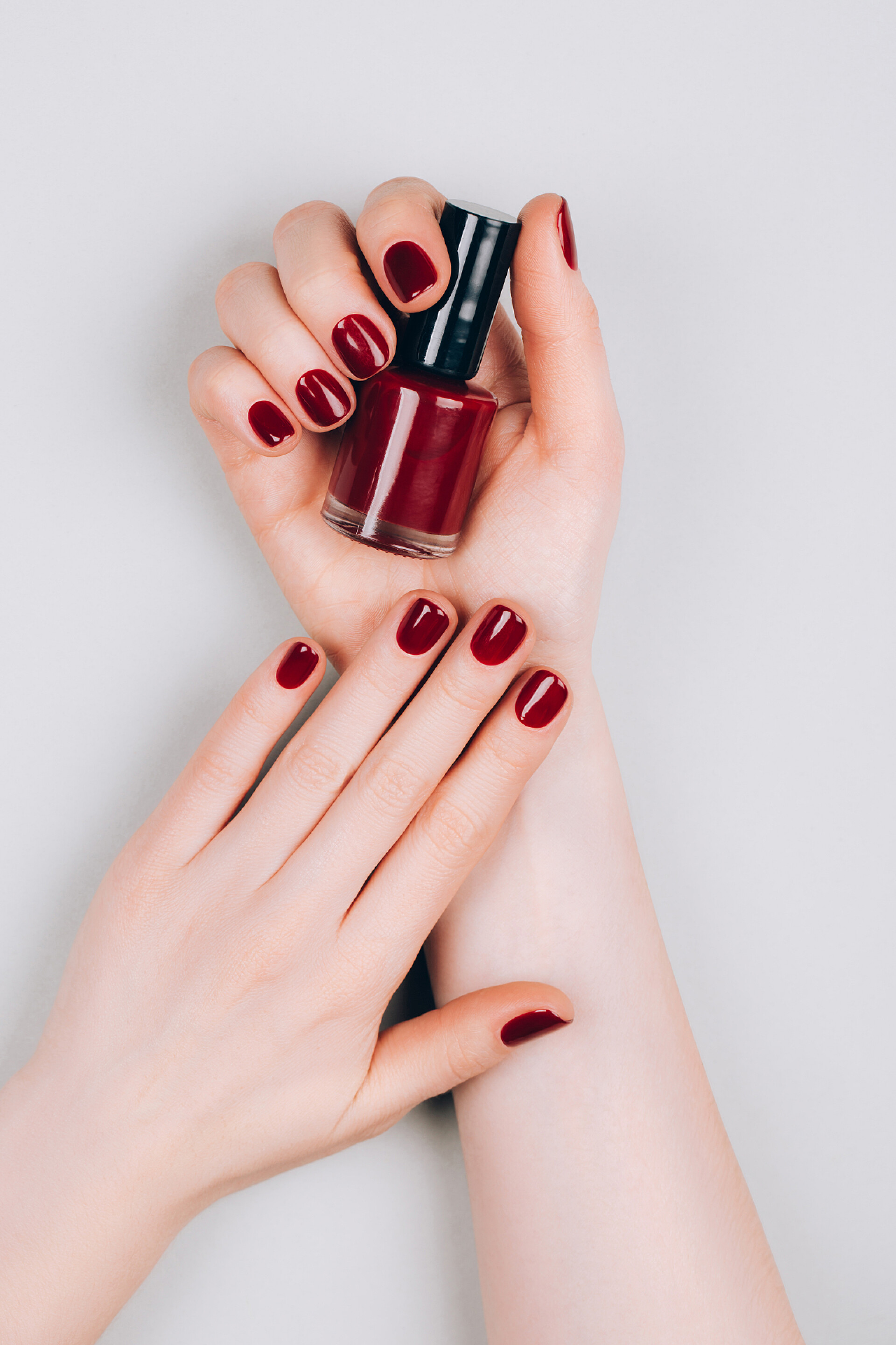 灰色背景上的漂亮的深红色指甲与一瓶指甲油漂亮的深红色美发与一瓶指甲油在灰色背景的手。程序概念。平铺风格.