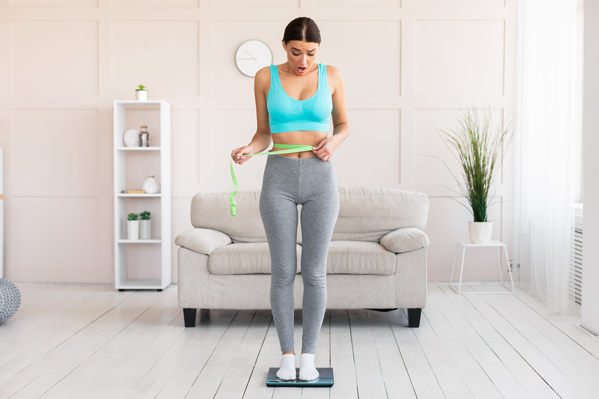 站在家里量腰围和体重的小女孩带着带子站在举重秤上的震惊女孩的腰围测量