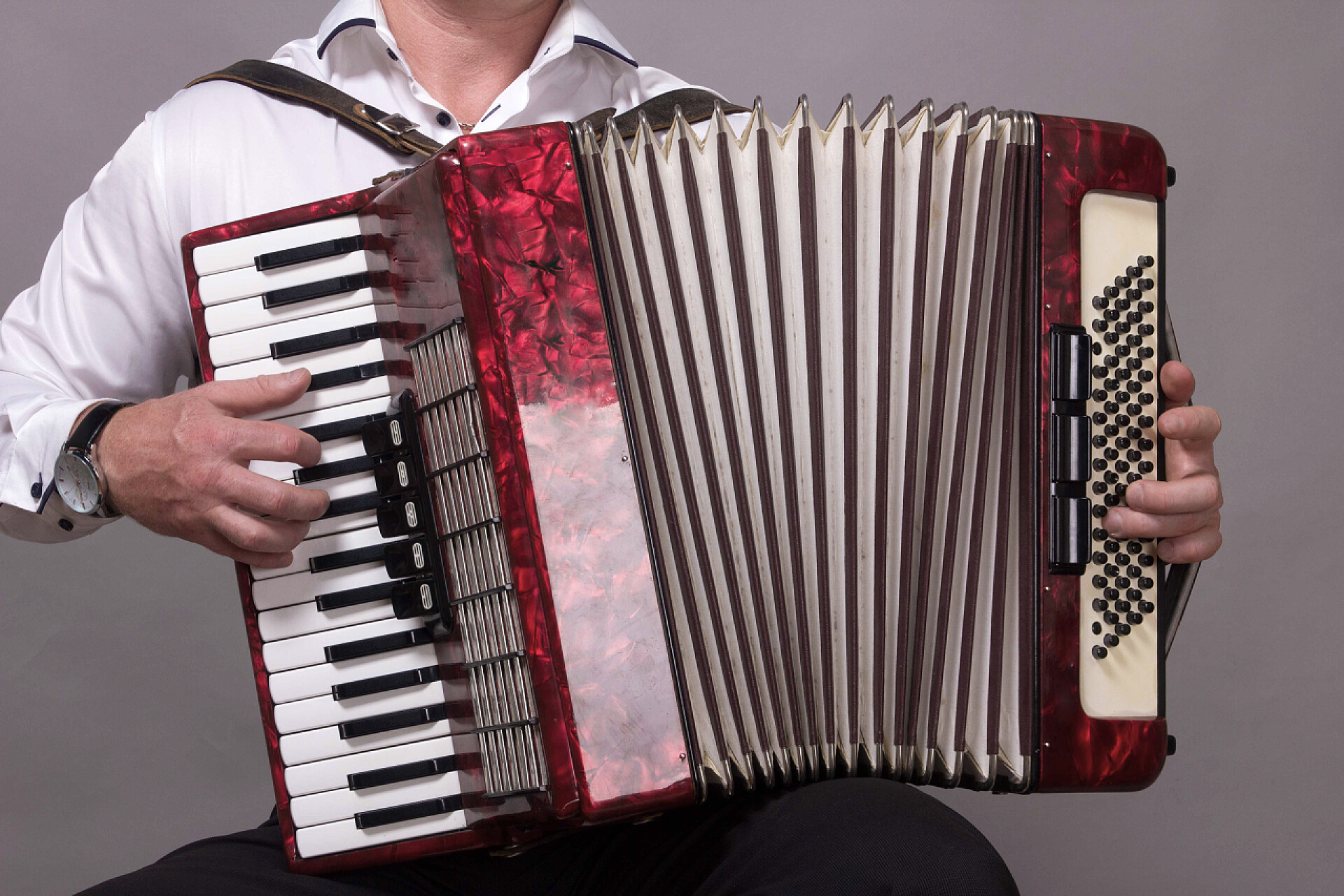 弹奏红色手风琴的男人一个穿着白衬衫、弹奏红色手风琴的男人的服装细节。手部特写