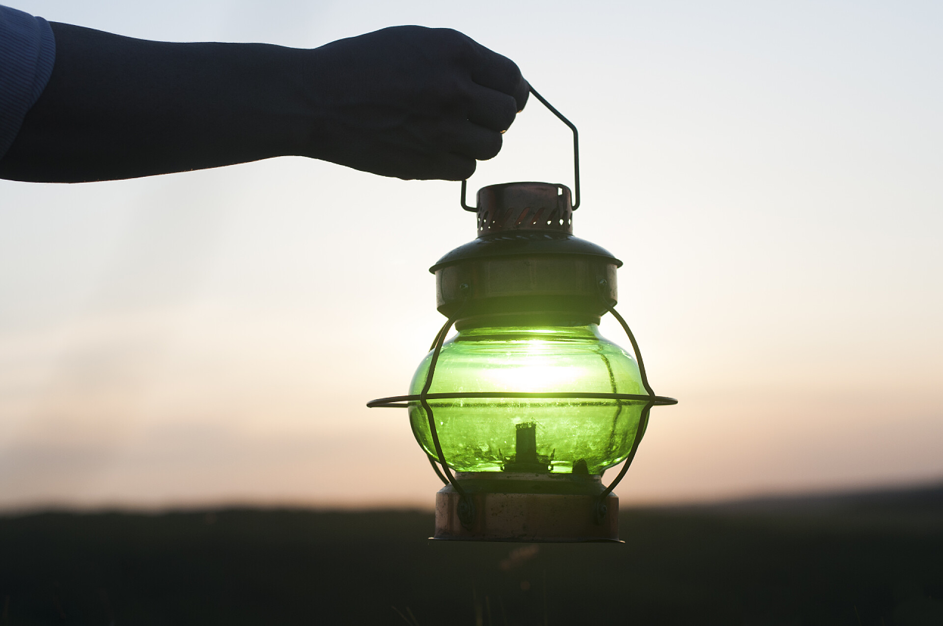 一只手拿着灯一只手拿着古董古董灯.背对着天空日落了灯具