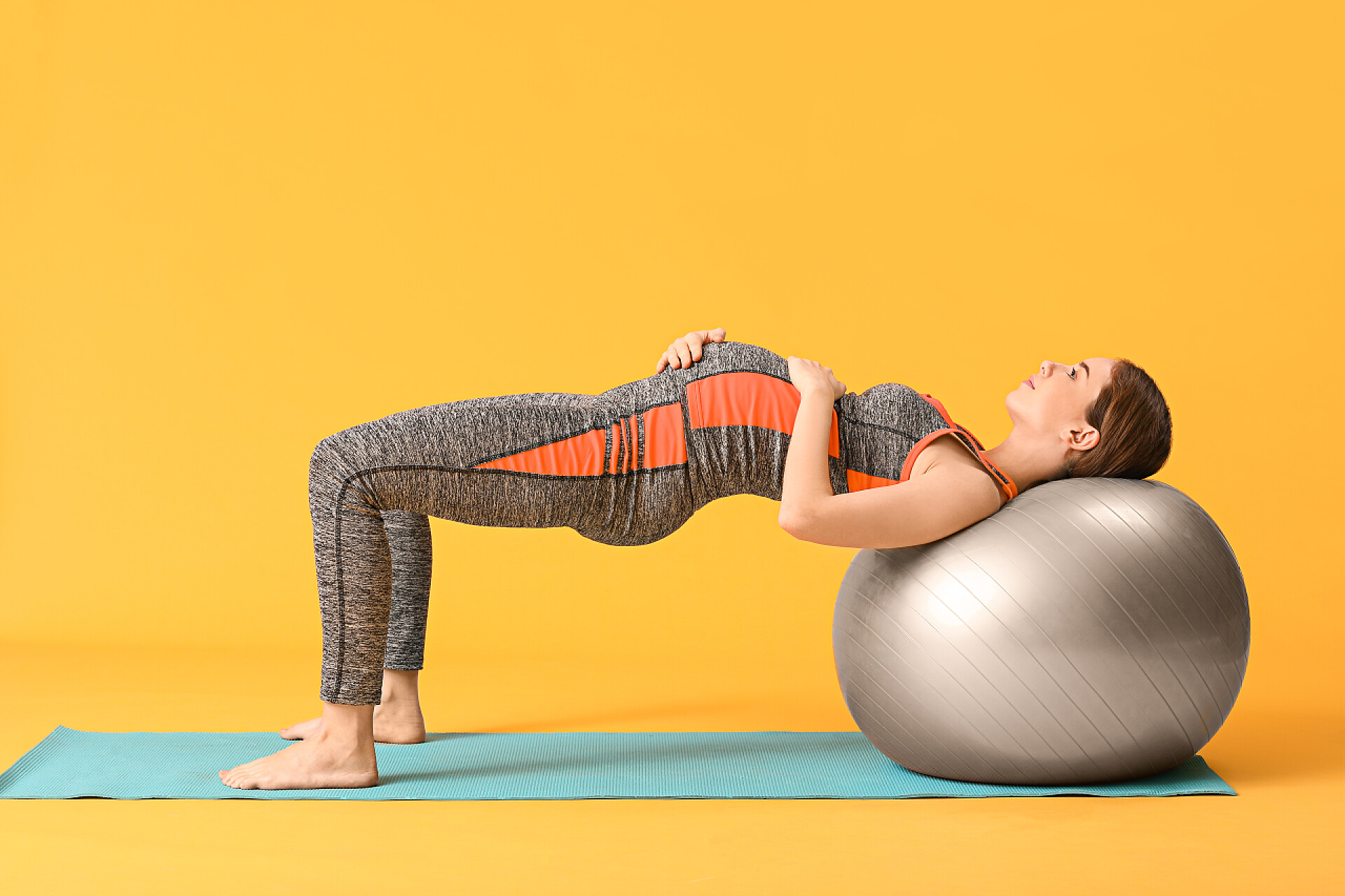 橙色背景上做瑜伽的孕妇年轻孕妇在有色人种背景下的培训