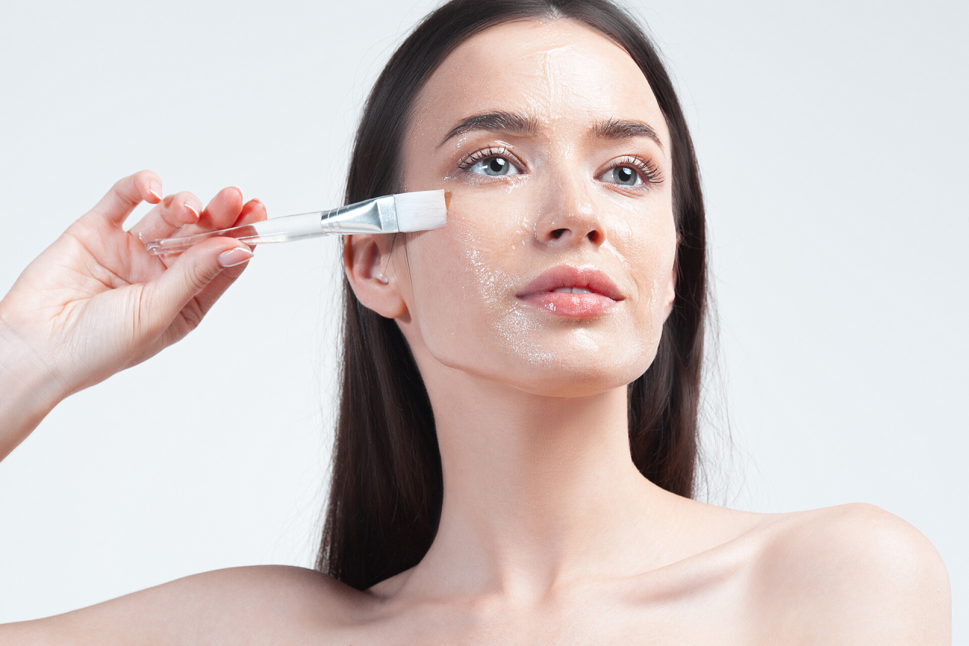 女人用刷子涂抹面膜年轻美丽的女人，皮肤洁白完美，用透明的保湿面膜刷妆容。皮肤护理和年龄化妆品概念