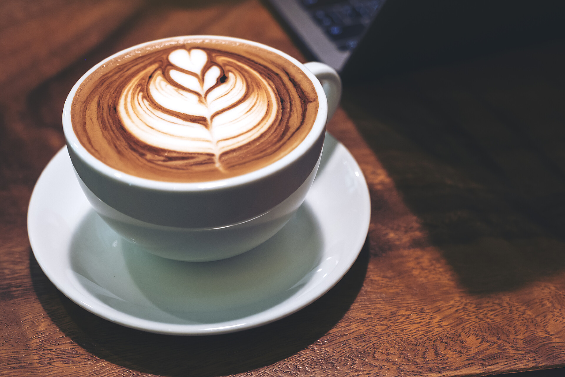 木桌上的拿铁咖啡木桌上挂着一杯热拿铁咖啡、拿铁艺术和笔记本电脑的特写镜头