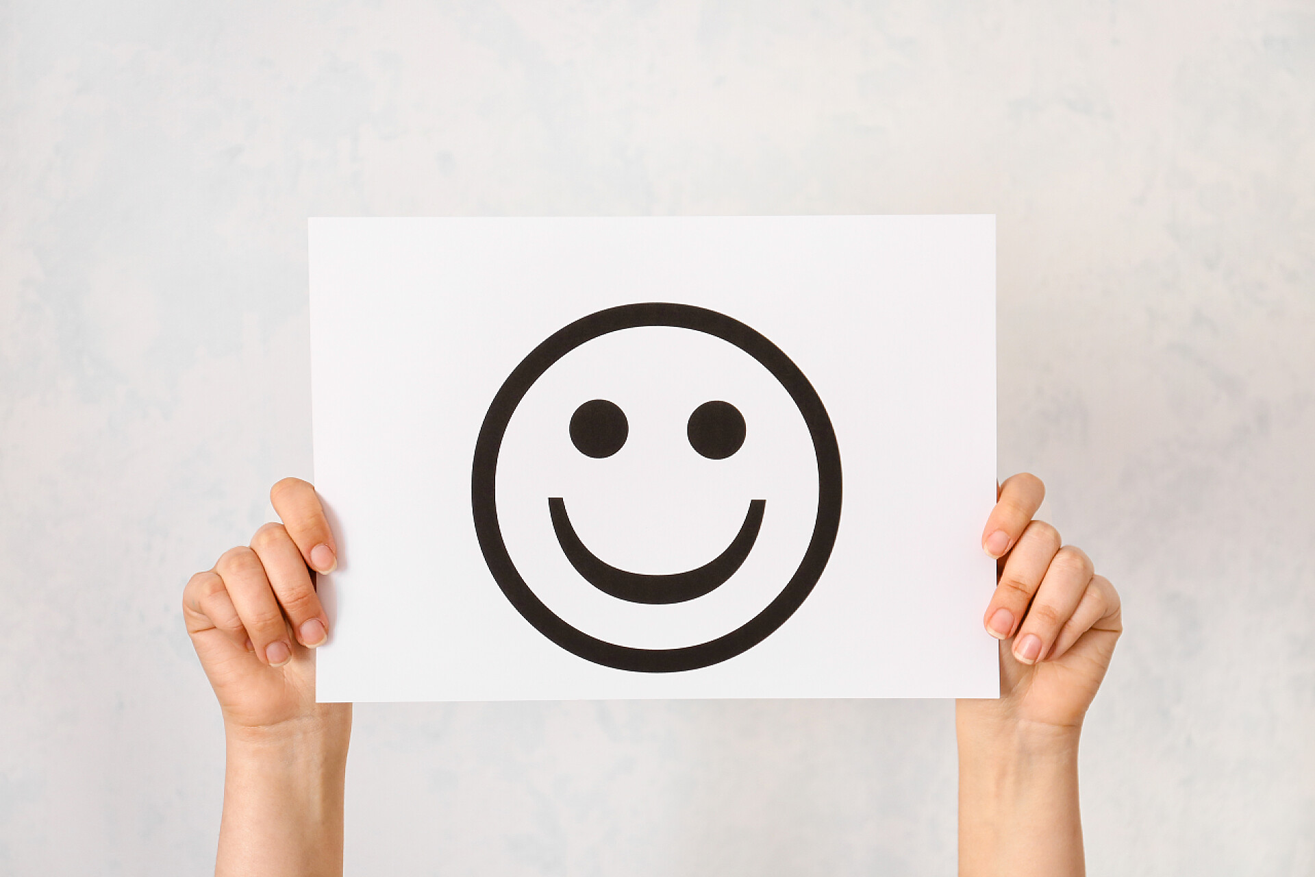手拿画在白纸上的黑色笑脸女性手拿着白底笑着的纸片