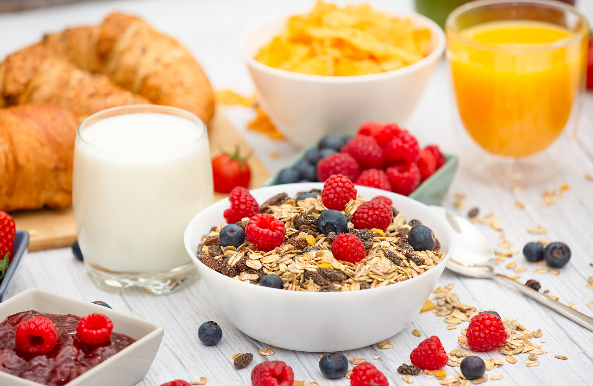 餐桌上丰盛的早餐早餐在早上享用，黄油羊角面包和玉米片全麦和葡萄干，牛奶在杯子里，草莓，蓝莓，覆盆子，猕猴桃，新鲜橙汁放在早餐桌上.