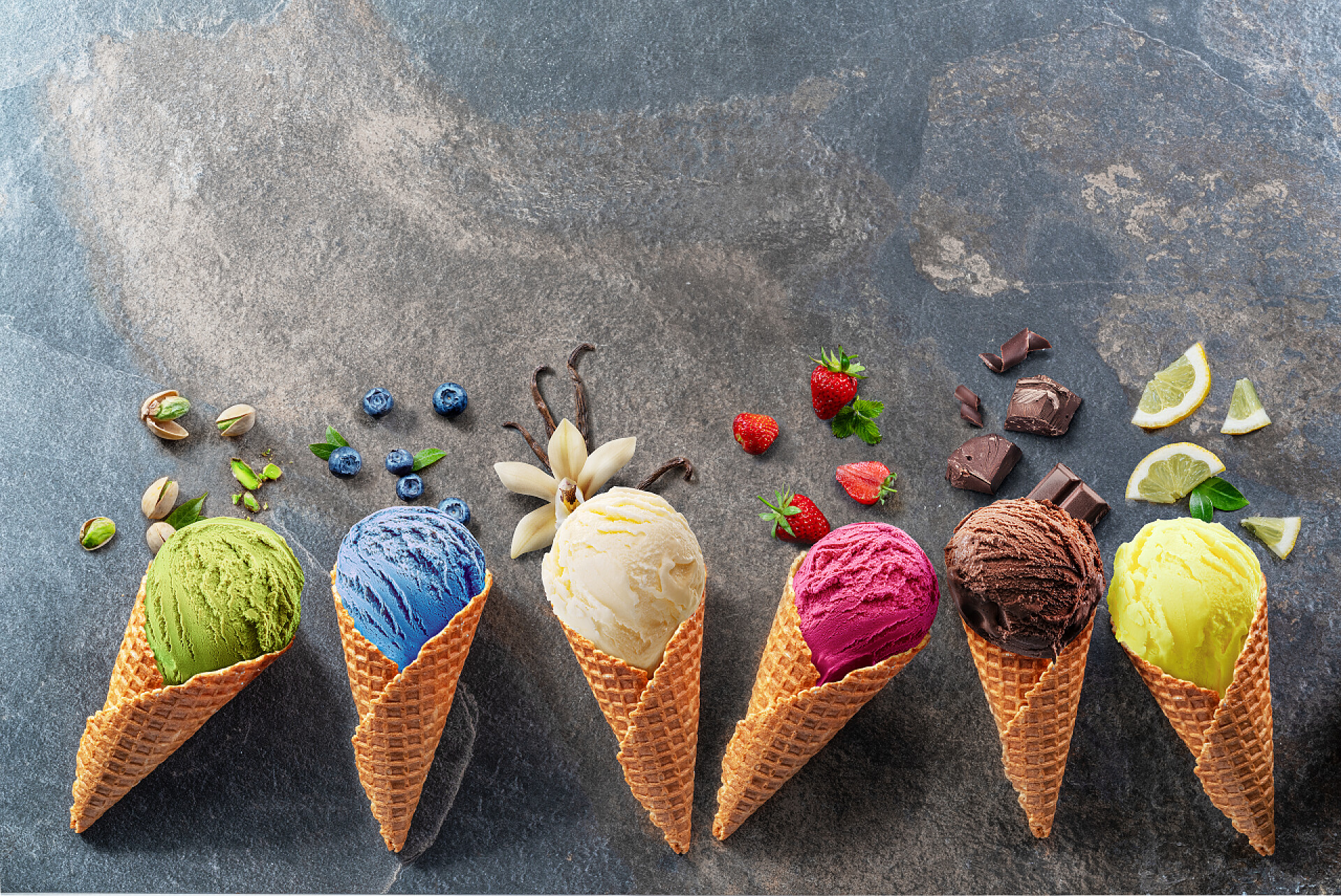 灰色背景上五颜六色的华夫饼蛋卷冰淇淋一套五颜六色的华夫饼蛋卷冰淇淋，其灰色背景上有水果片。阐述观点.
