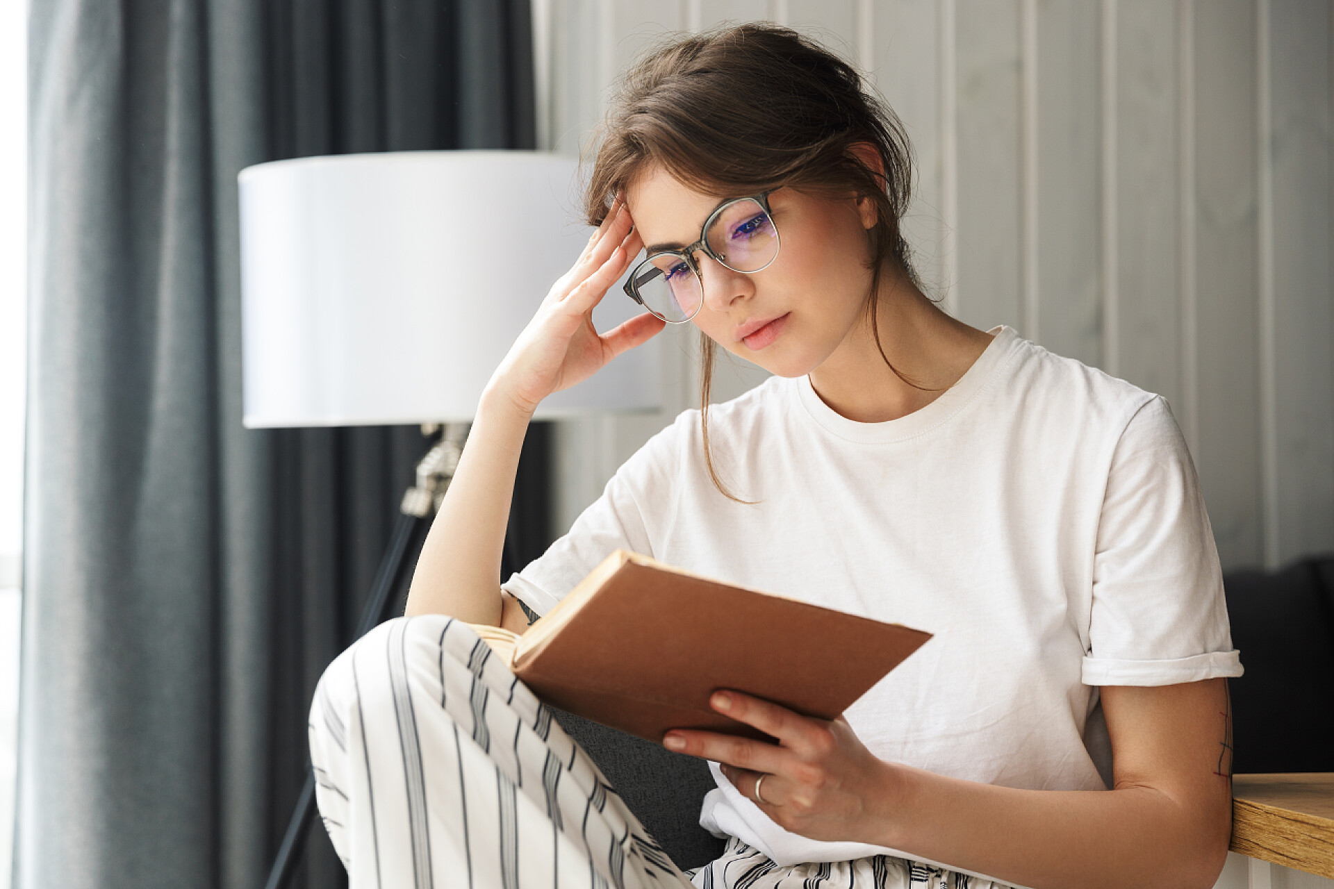 戴着眼镜的年轻女子在看书坐在舒适的房间里，戴着眼镜看书的年轻女子的照片