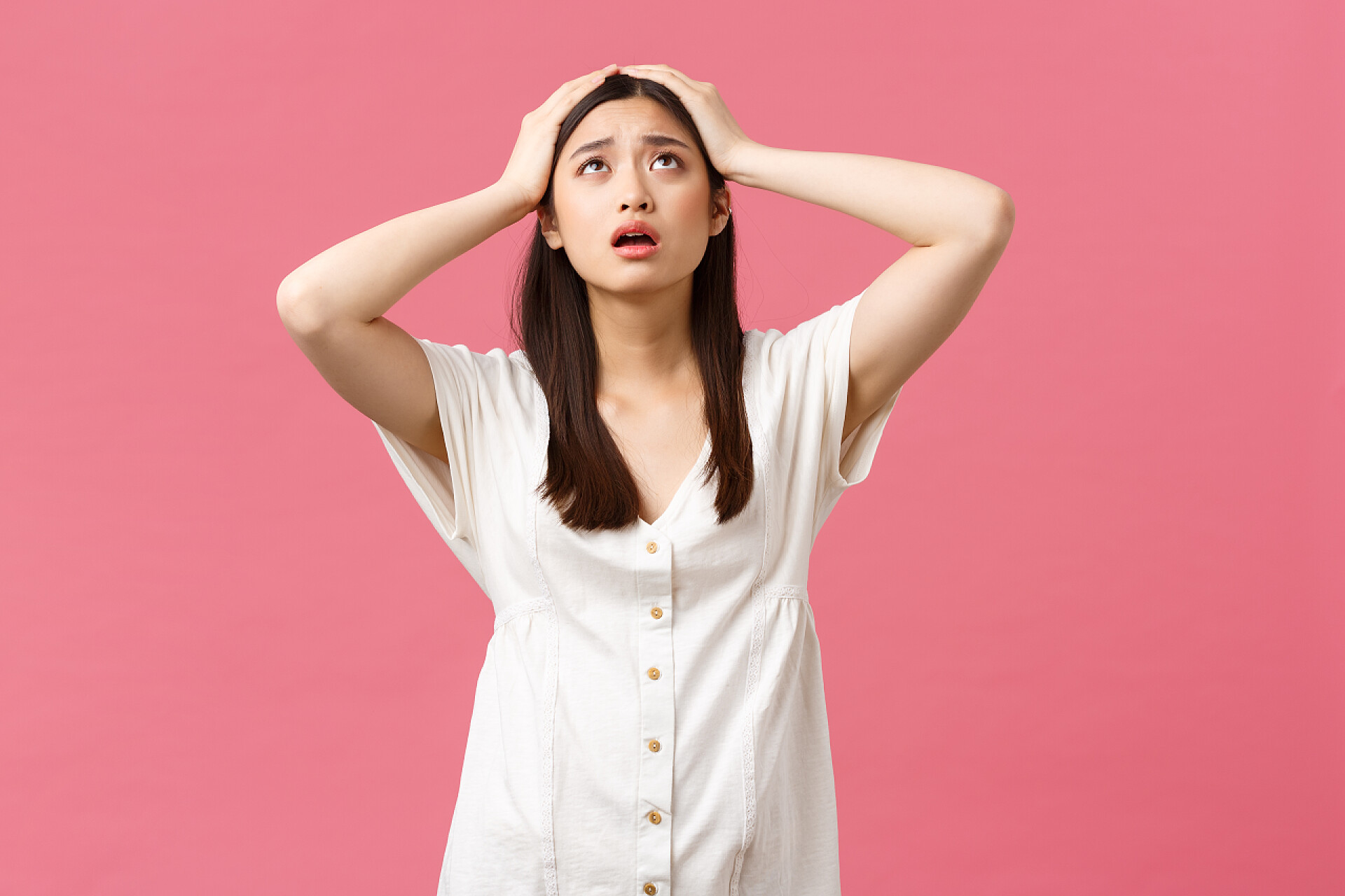 粉色背景中一个美丽的女人抱着脑袋很绝望美丽、人的情感和夏天的休闲观念.绝望而沮丧的年轻亚洲女人惊慌失措，望着天空，亲爱的上帝帮助，抓起头惊慌失措，焦虑地站在粉红的背景上