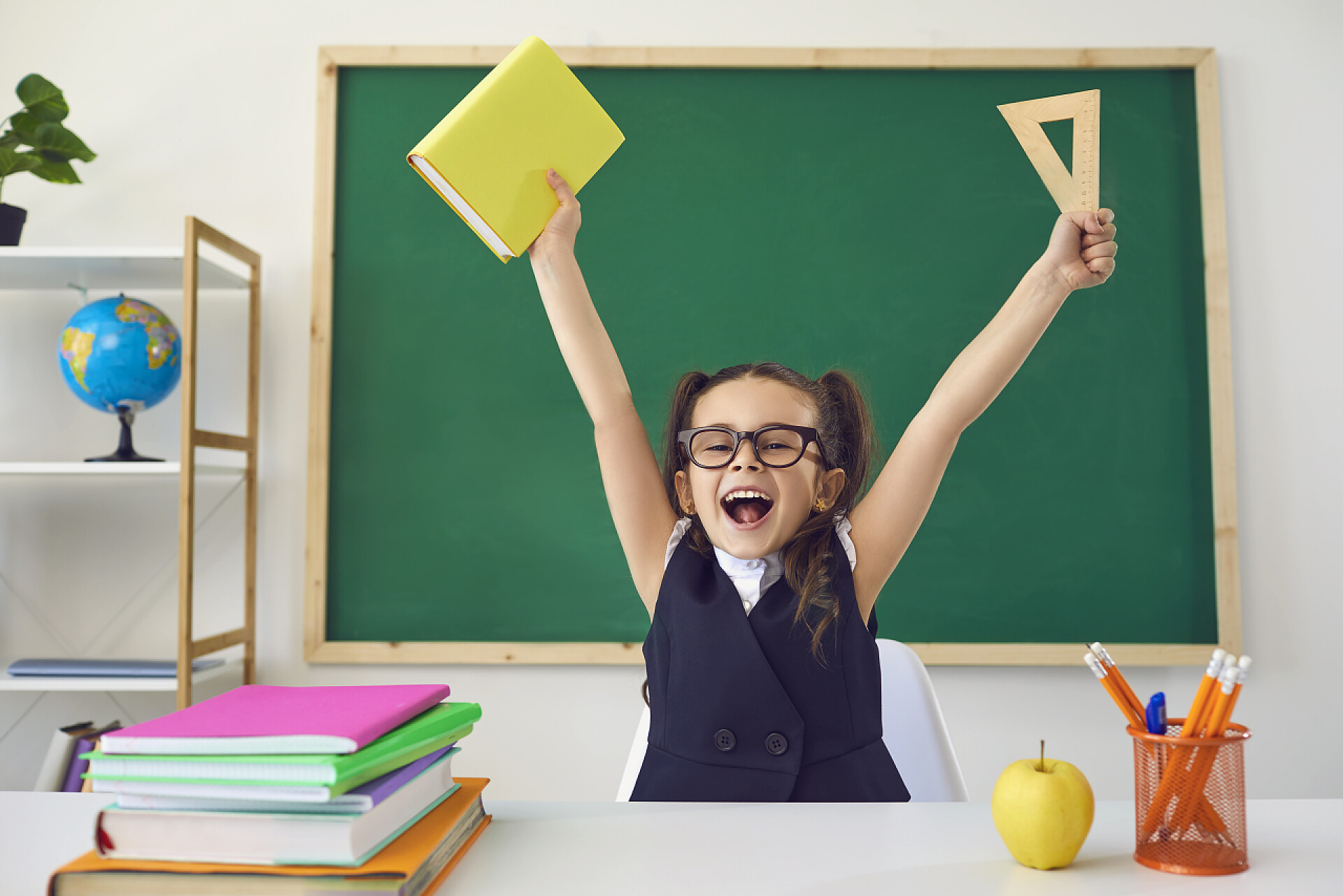 一个小女孩在黑板前高兴的举起了手回学校去一个快乐的小女生在教室的一块绿色黑板的后面举手表决.