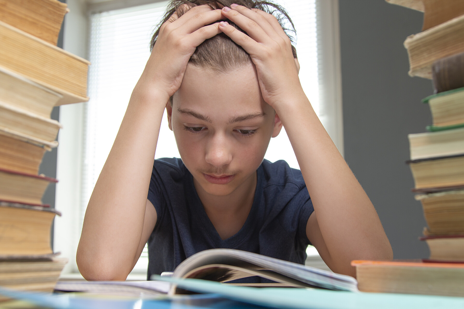 书桌前抱头思考的小男孩一个心烦意乱的学童在课本上做作业的画像