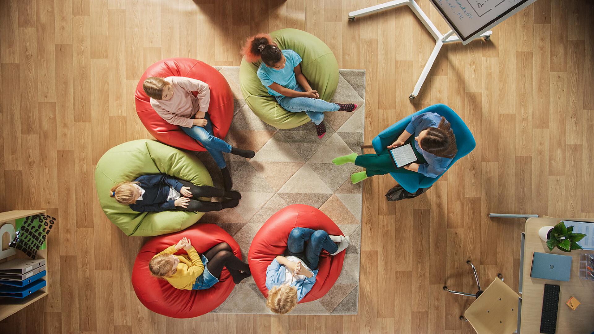 教室里坐在豆袋沙发上上课的老师和学生们的俯视图小学创意课堂：孩子们坐在豆袋上，老师给他们讲解课时，使用数码平板电脑。顶视图射击