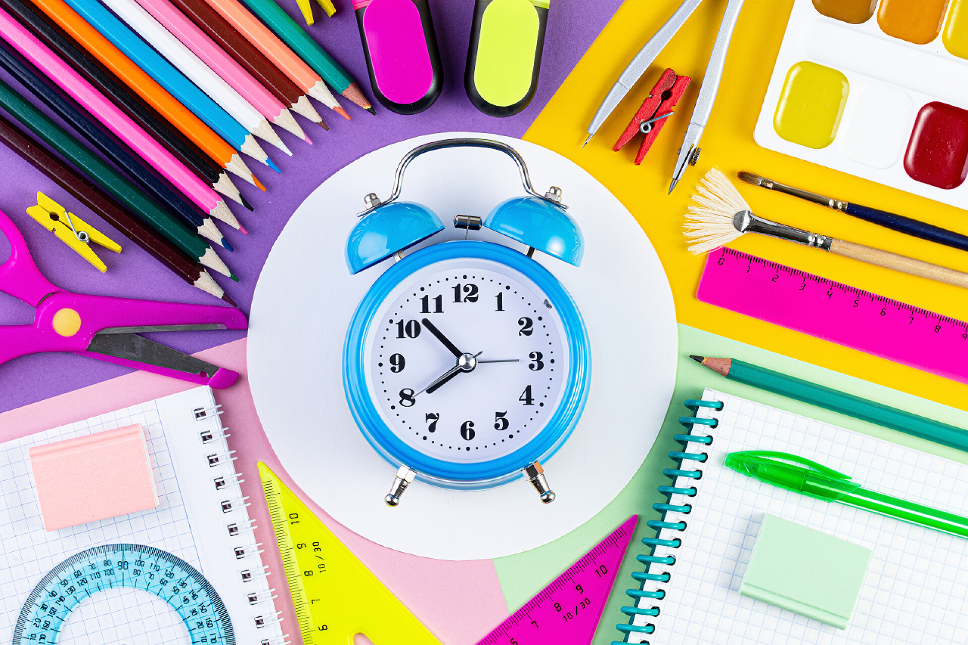 桌面上彩色文具和闹钟的顶视图创意扁平放置顶部视图回到学校的概念与闹钟.固定的，回到学校，暑假，教育观念。彩色学校用品的纸张背景。文本或设计模板