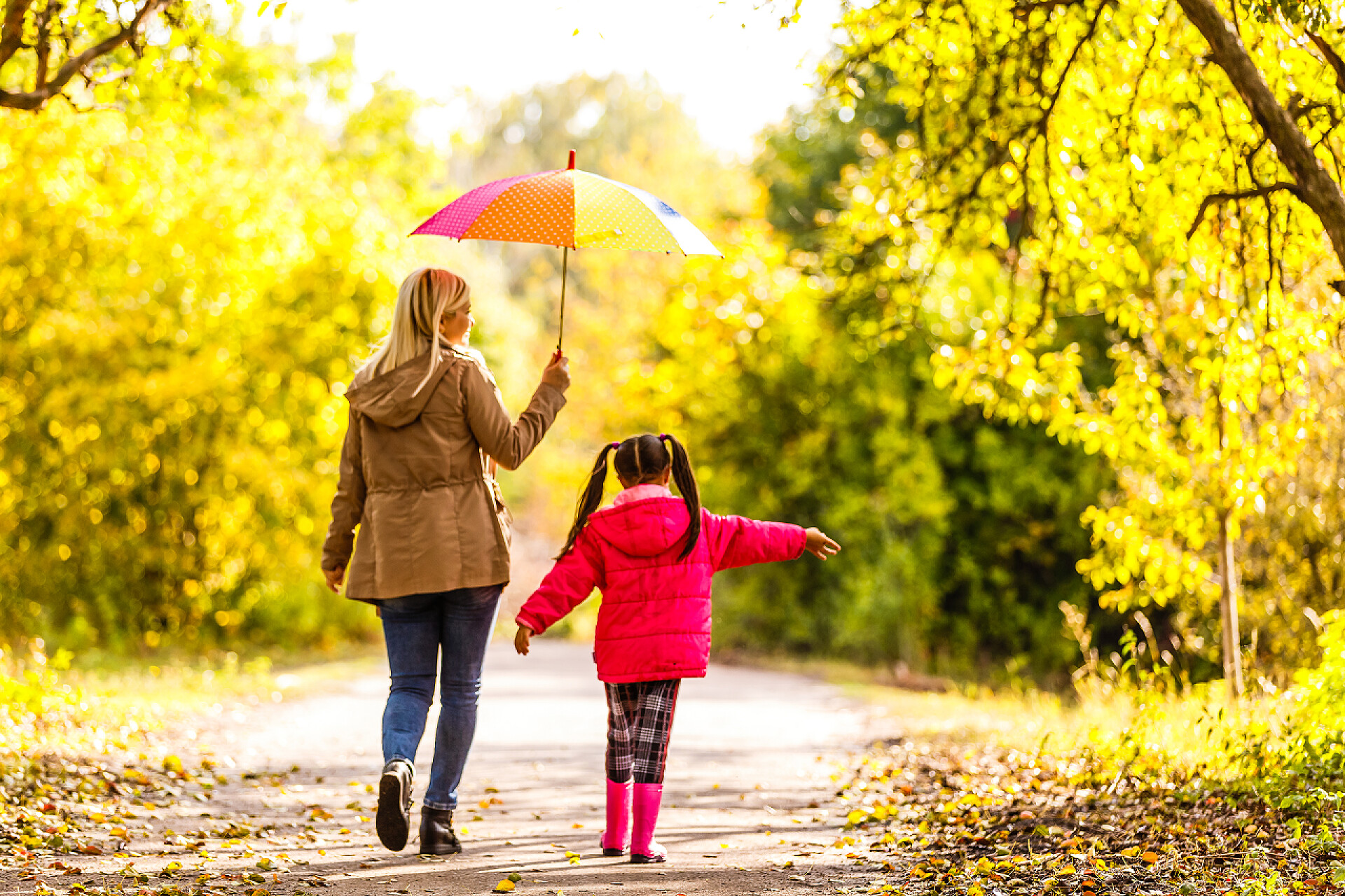 春天森林里打伞遮阳行走在小路上的母女妈妈和女儿带着雨伞在春巷里