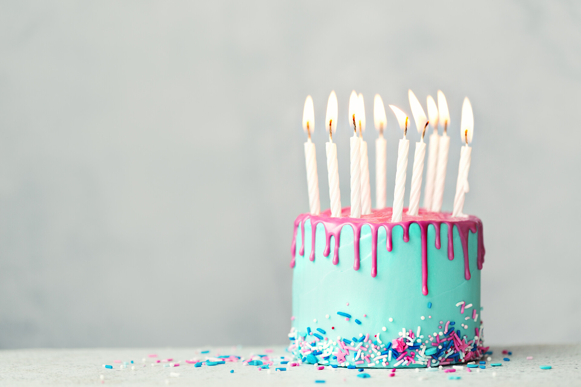 桌子上插满蜡烛的生日蛋糕特写生日蛋糕，上面有蓝色的糖霜，粉红色的水滴和十支白色的生日蜡烛