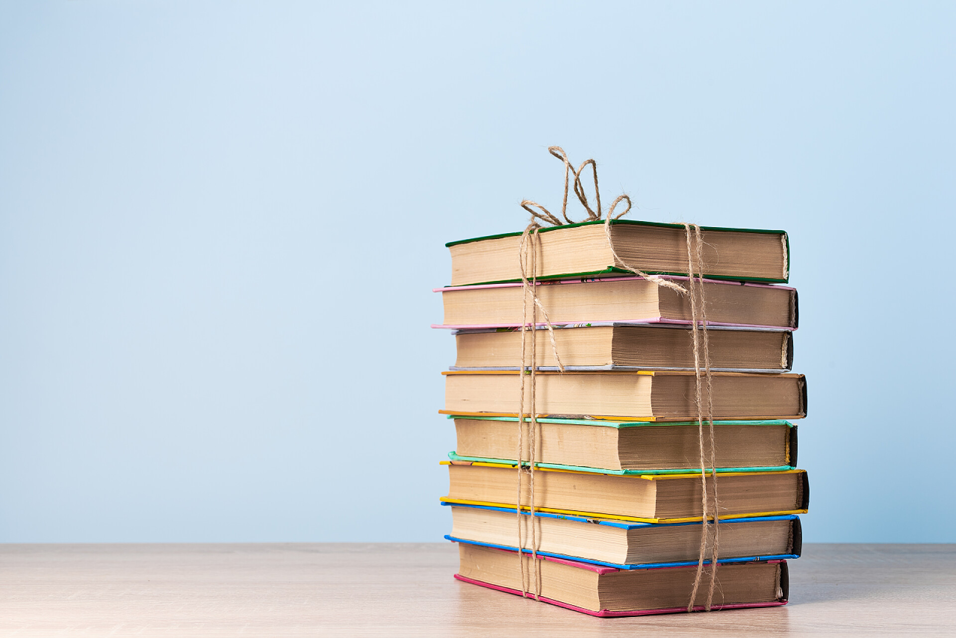 桌子上用绳子捆绑着书的特写一堆乱糟糟的书，用绳子拴在一张木制桌子上，靠着一堵浅蓝色的墙，留有空余的文字空间