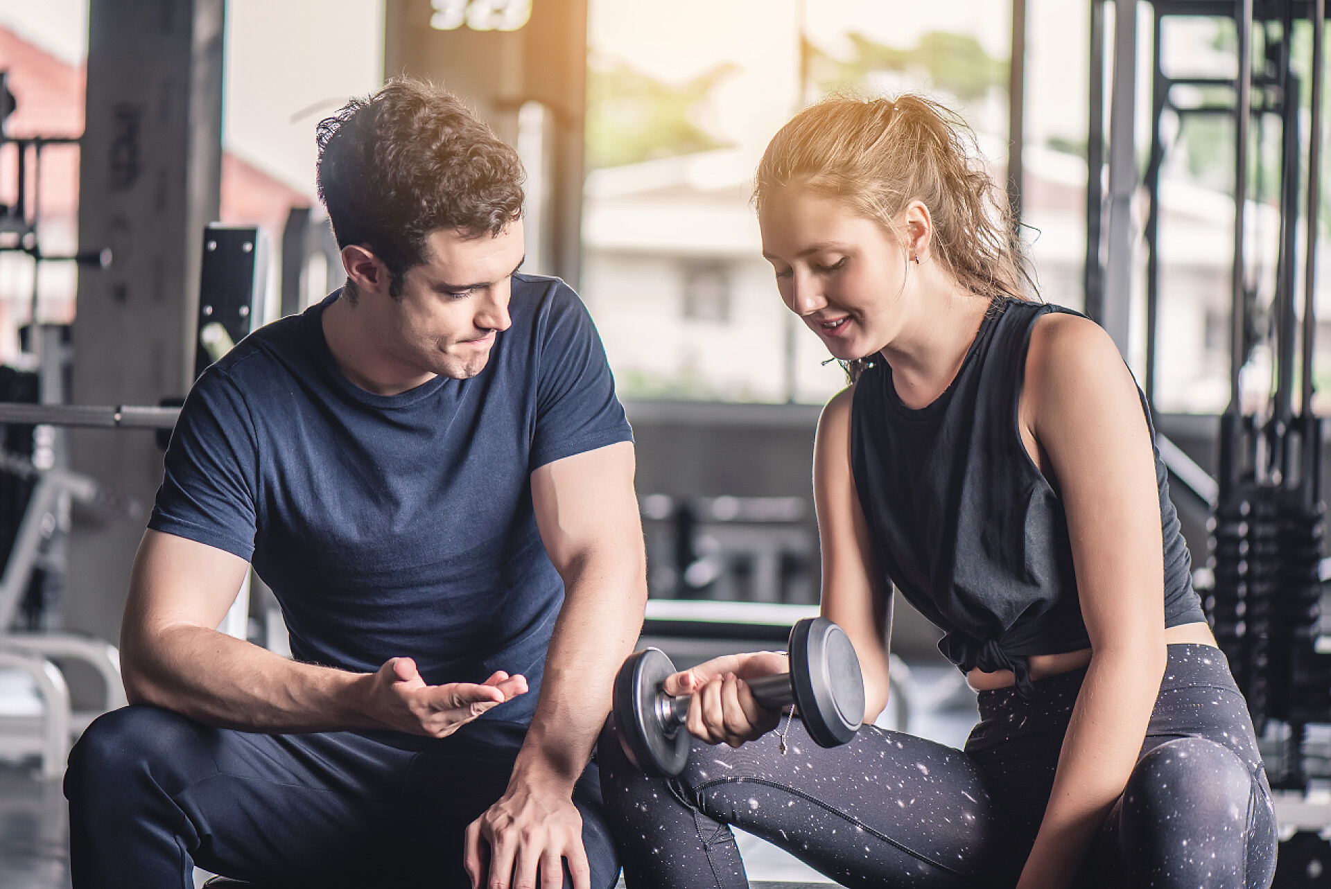 健身房里男教练正教女学员抬哑铃体操馆教练用哑铃进行年轻貌美女子运动的电影基调.  