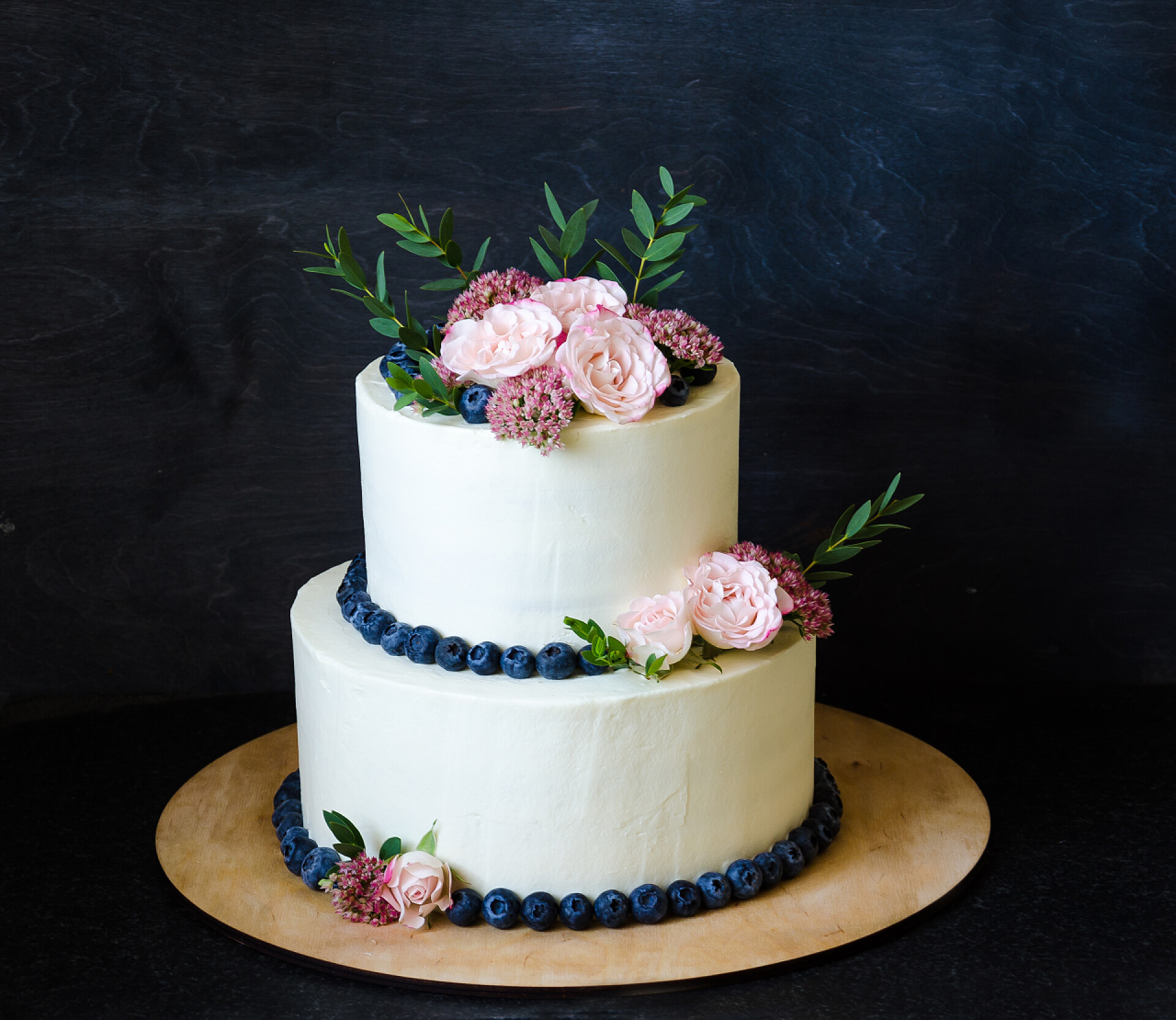 黑色背景上的两层婚礼奶油芝士蛋糕两层婚礼奶油芝士蛋糕，配上玫瑰和蓝莓