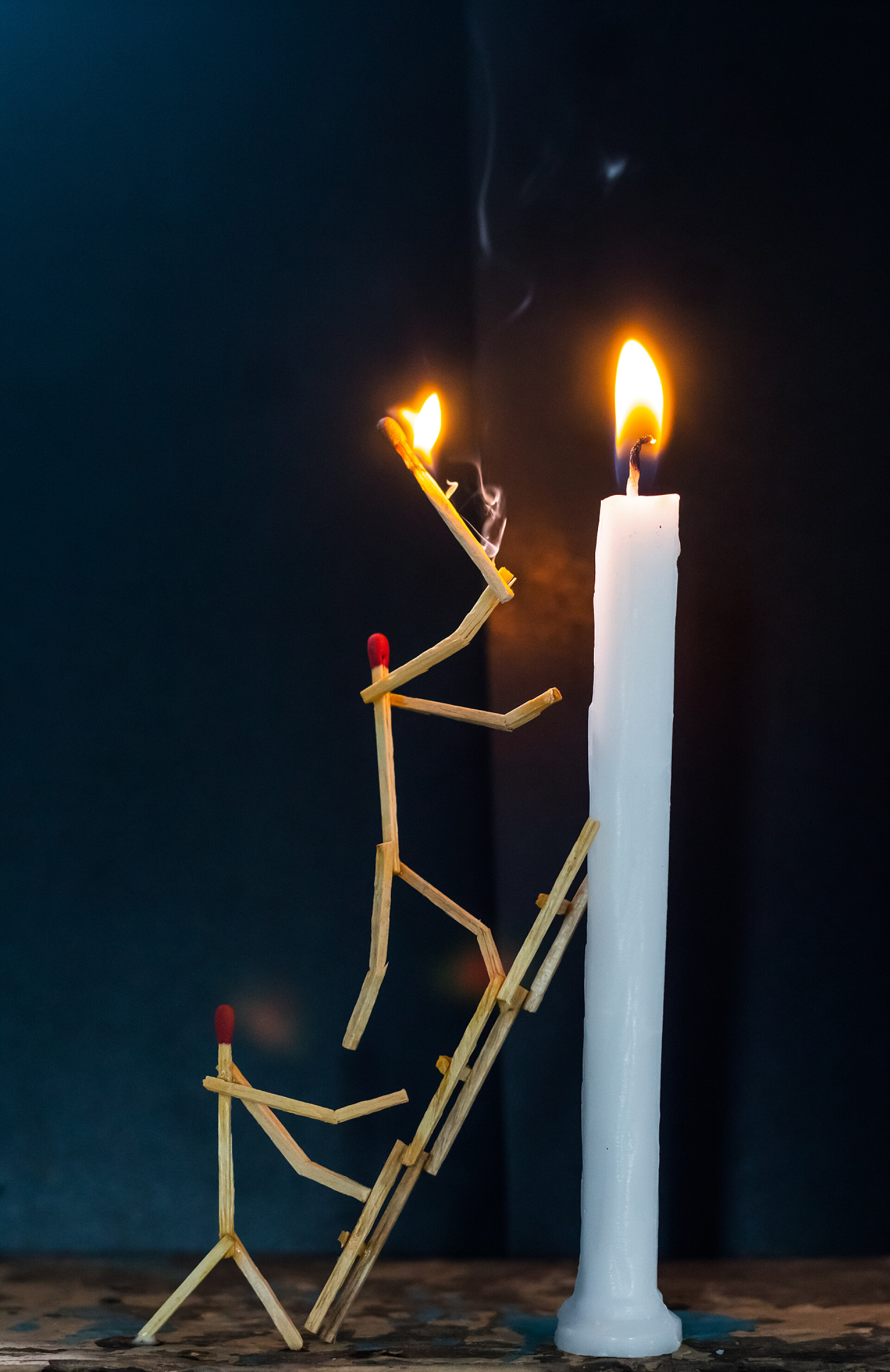 黑色背景上的蜡烛和人形状的火柴火柴棍的形状是男人点燃蜡烛，火柴棍的形状是男人点燃蜡烛.