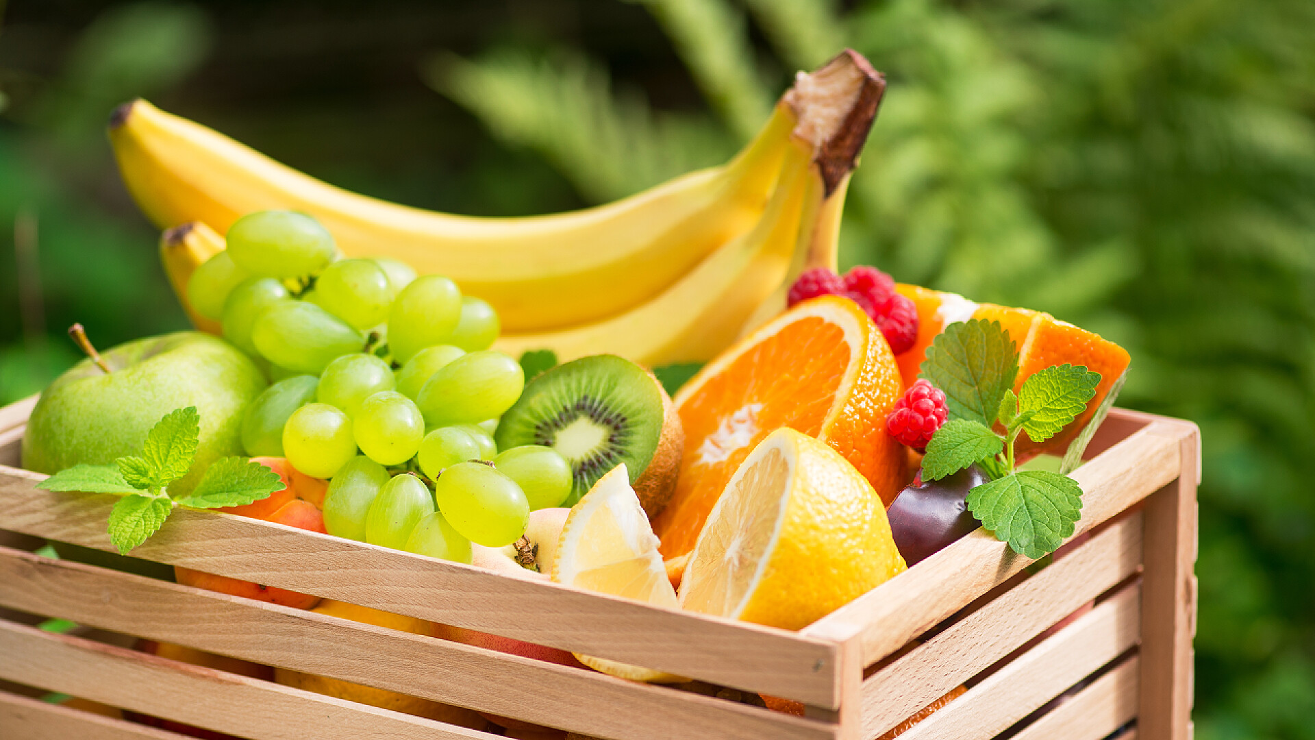 木筐上的水果一筐新鲜的水果,有香蕉,苹果,葡萄,绿色的猕猴桃在花园的背景.健康及维他命食物。夏季收获.