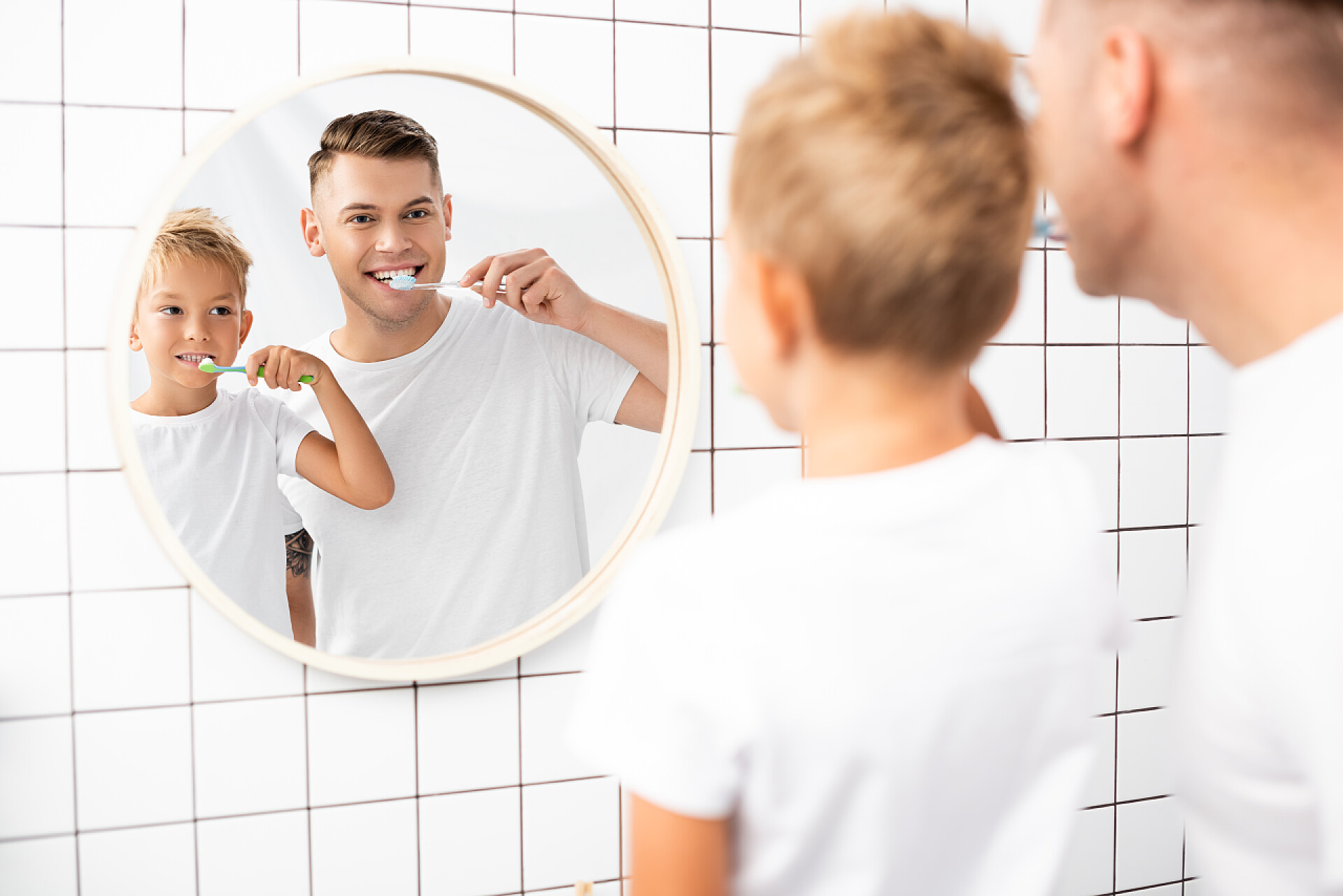 父子在浴室里对着镜子刷牙快乐的父亲和儿子一边刷牙，一边看着浴室里的镜子，前景暗淡