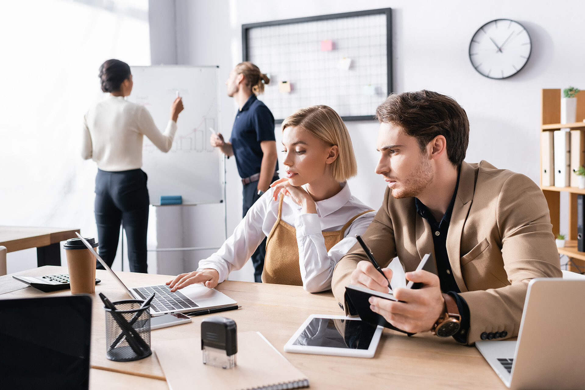 四个年轻人在办公室里鼻子疼专心致志的男人在笔记本上写作，而坐在女人身边的男人在办公室的笔记本电脑上打字，背后是模糊的多元文化同事